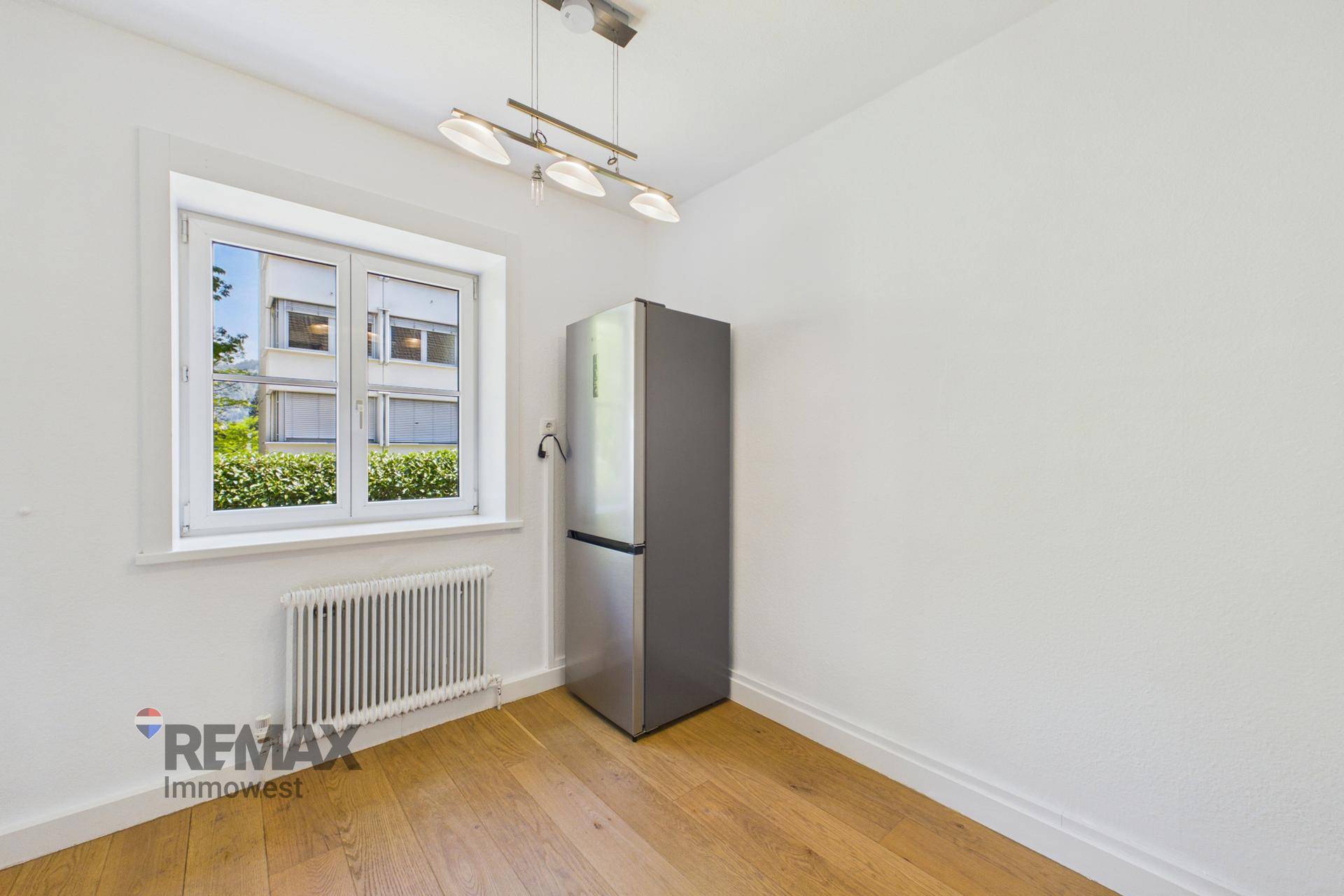 Heller Raum mit Fenster, Heizkörper und einem freistehenden Kühlschrank, ideal als Essbereich.