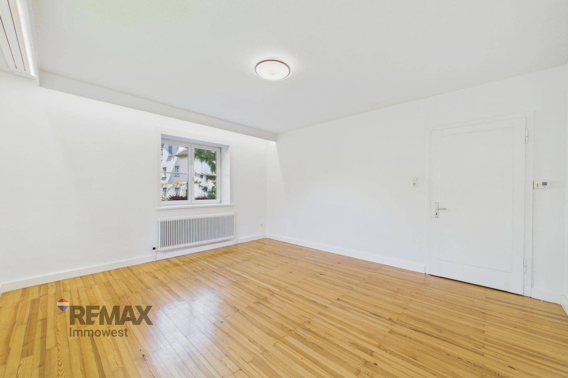 Helles Schlafzimmer mit Fenster, Heizkörper und klassischem Holzfußboden, bietet eine gemütliche Atmosphäre.
