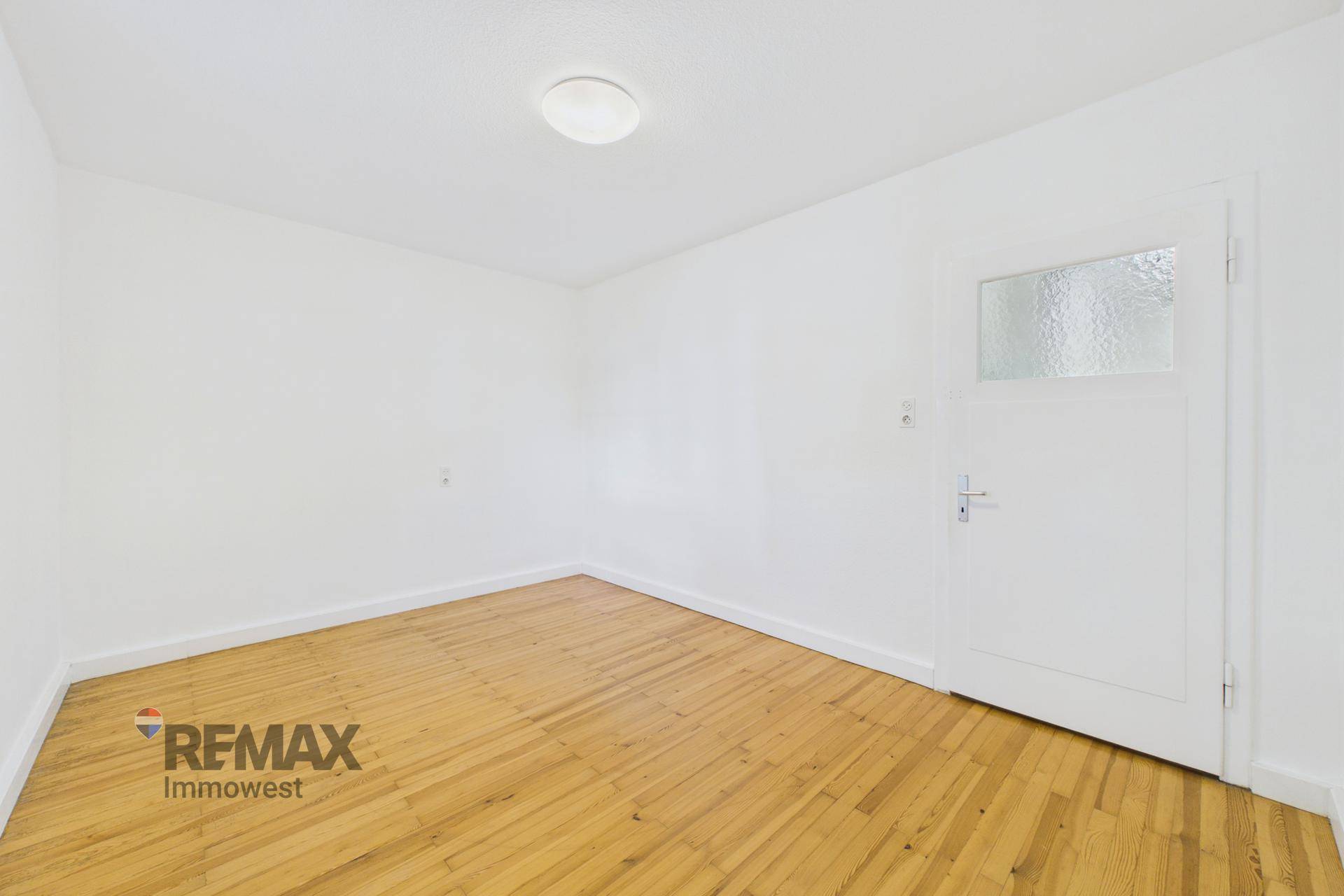 Schlichtes Zimmer mit Holzfußboden und einer Tür mit Glaseinsatz, bietet Privatsphäre und Licht.