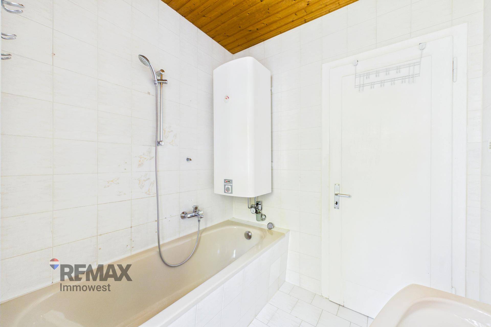 Funktionales Badezimmer mit Badewanne, Duschvorrichtung und gefliesten Wänden, sowie Holzdecke.