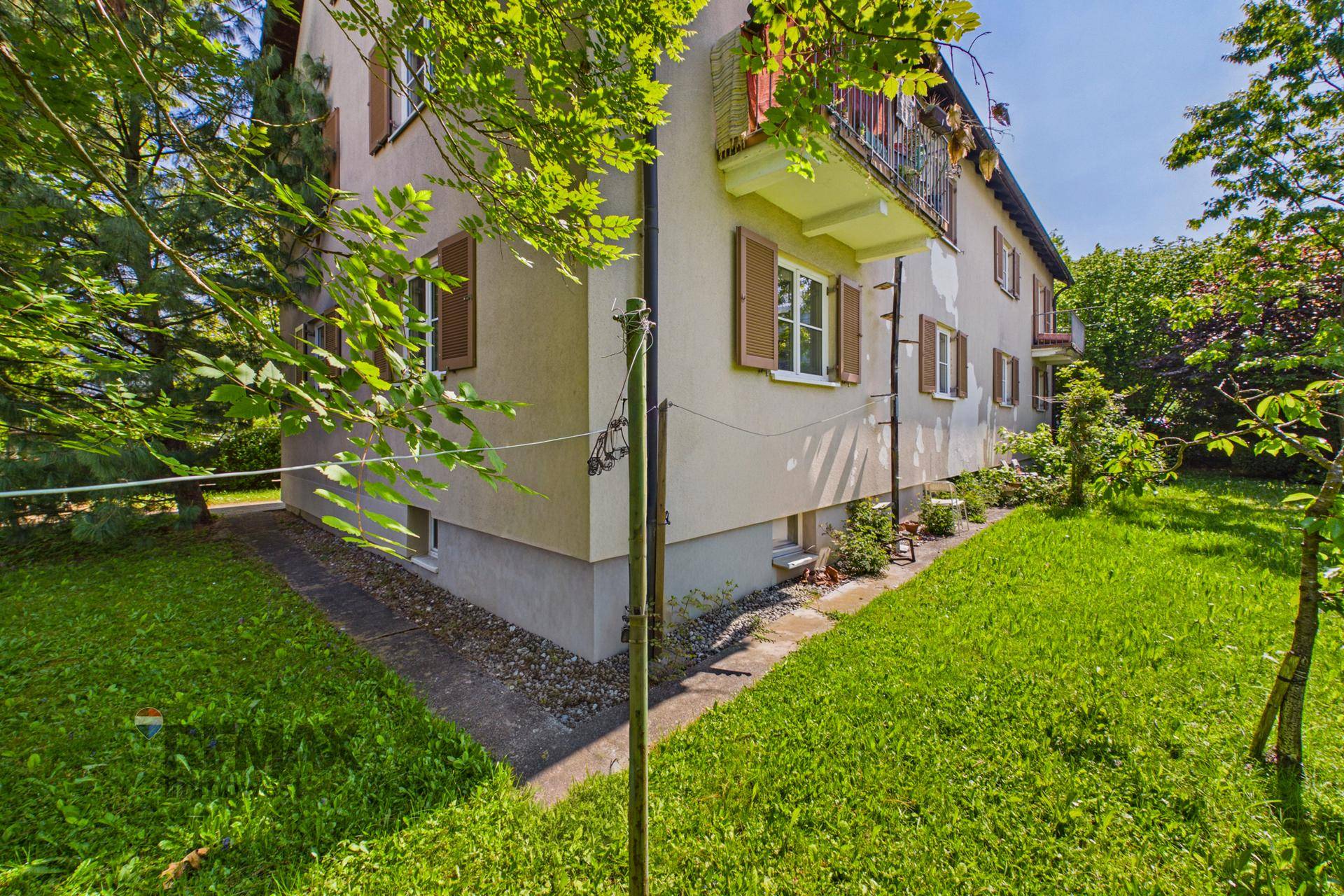 Seitenansicht des Gebäudes mit kleinem Balkon und angrenzendem, gepflegtem Gartenbereich.