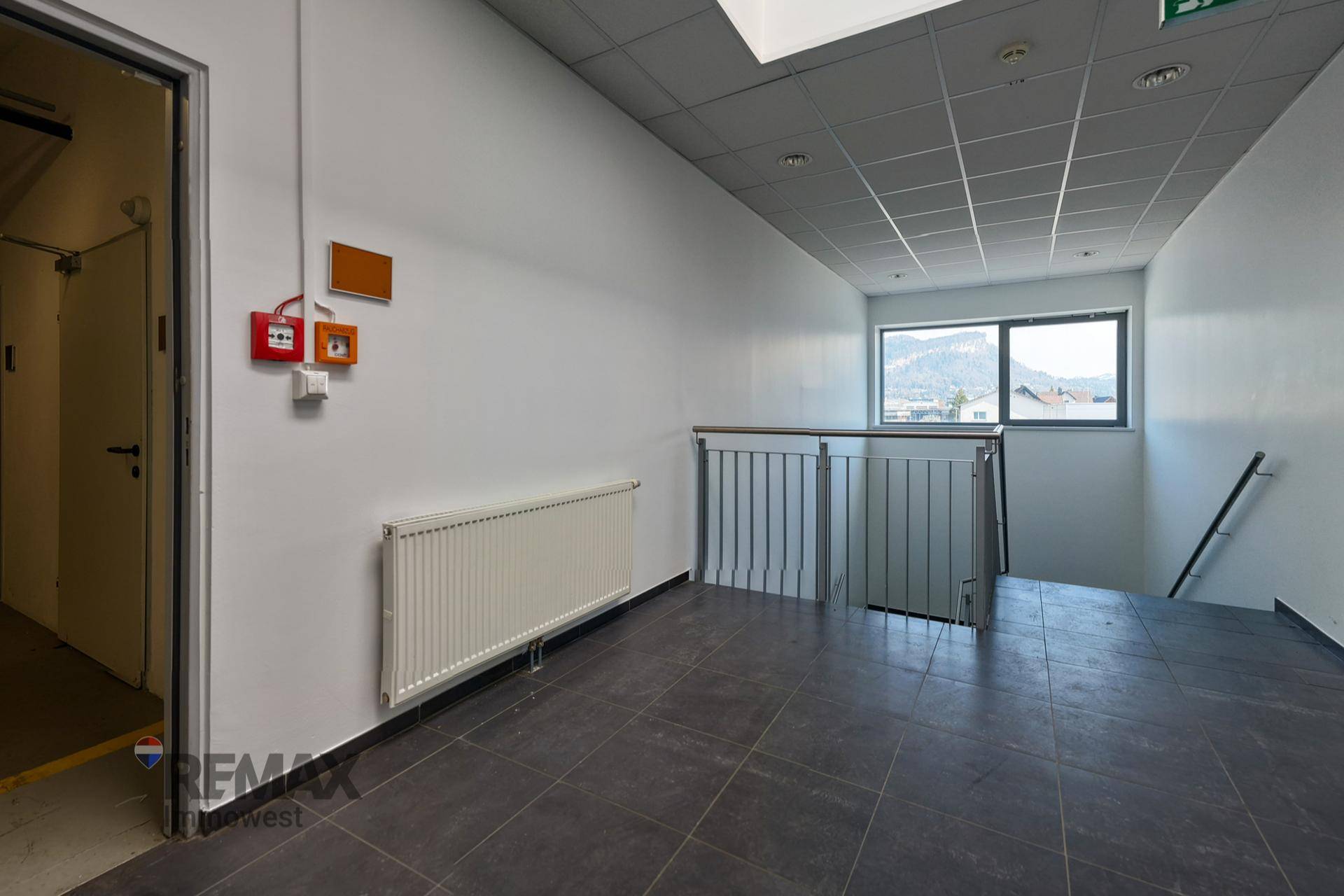 Treppenabsatz mit dunklem Fliesenboden, Fenster mit Bergblick und Heizkörper.