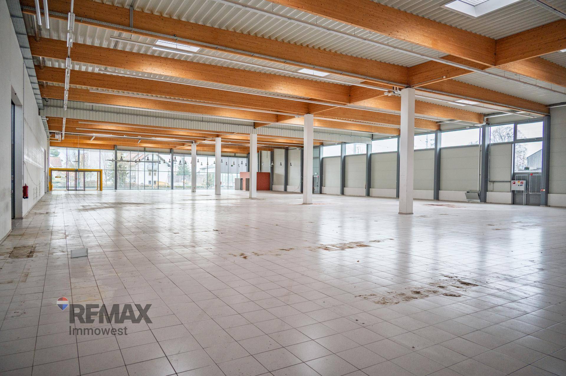 Große, leere Lagerhalle mit hohen Holzdecken, Fliesenboden und viel Tageslicht durch Fenster.