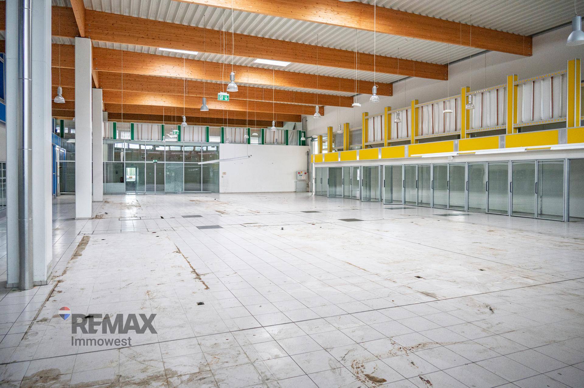 Weitläufige Lagerhalle mit hohen Decken, Holzbalken und gelben Regalsystemen an der Seite.