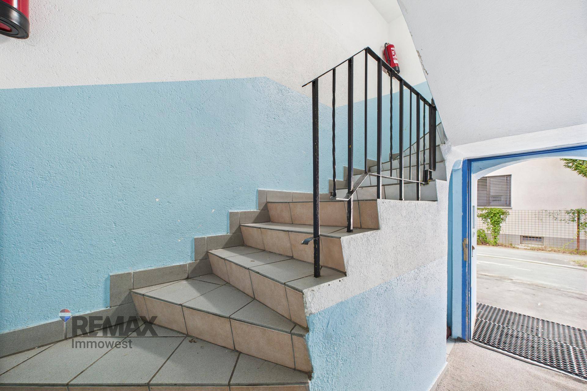 Eingangsbereich mit gefliester Treppe, blau-weißen Wänden und schmiedeeisernem Geländer.