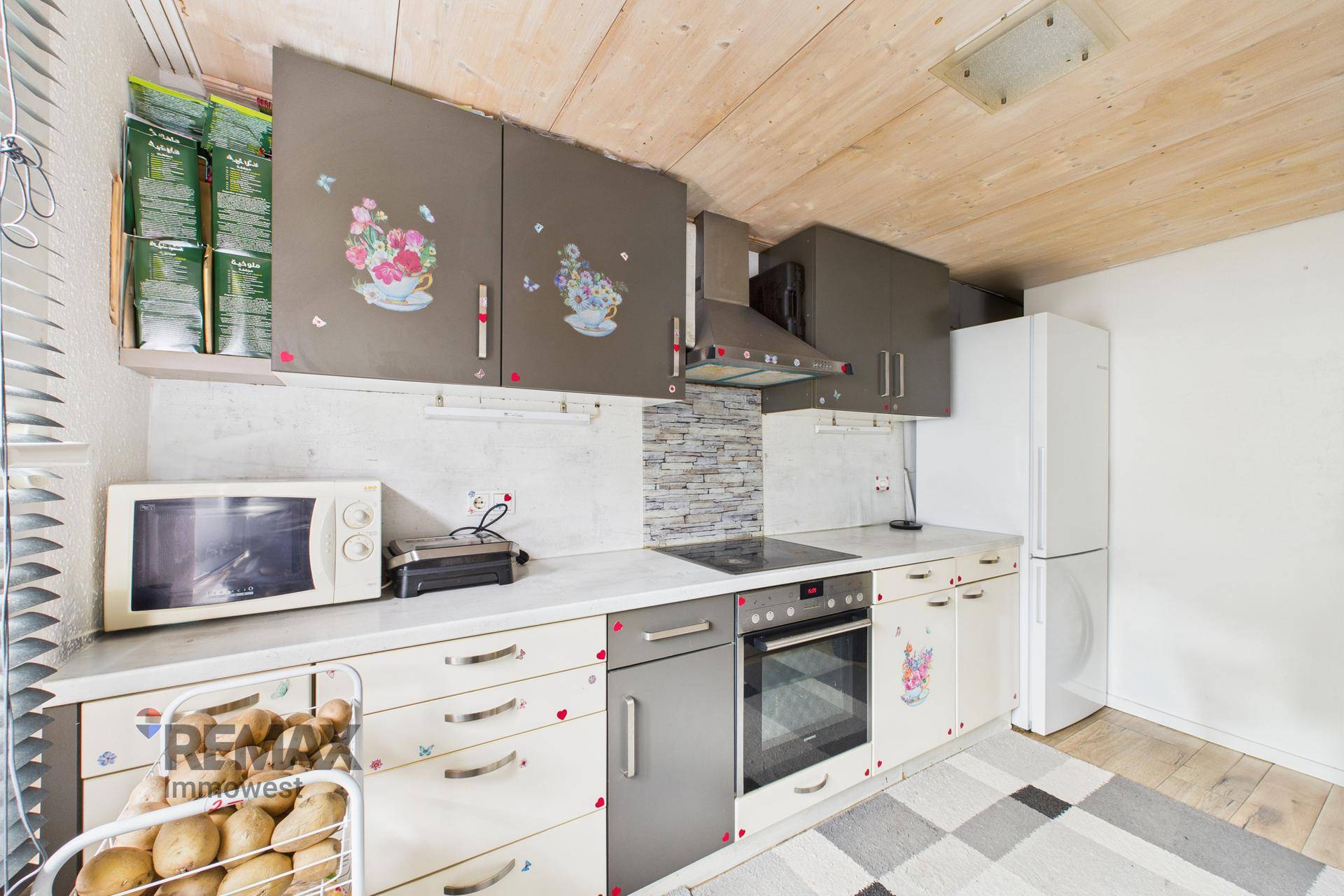 Küche mit Holzdecke, bunten Schränken, integriertem Backofen und freistehendem Kühlschrank.