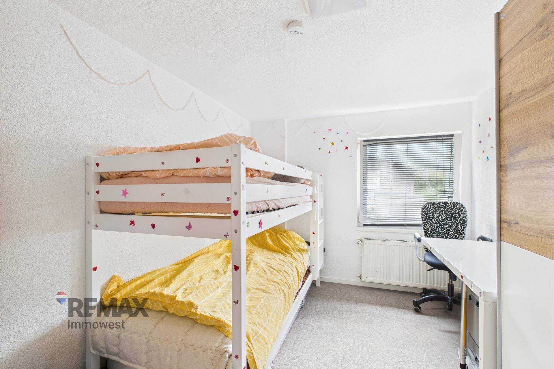 Helles Kinderzimmer mit Etagenbett, Schreibtisch und Teppichboden.