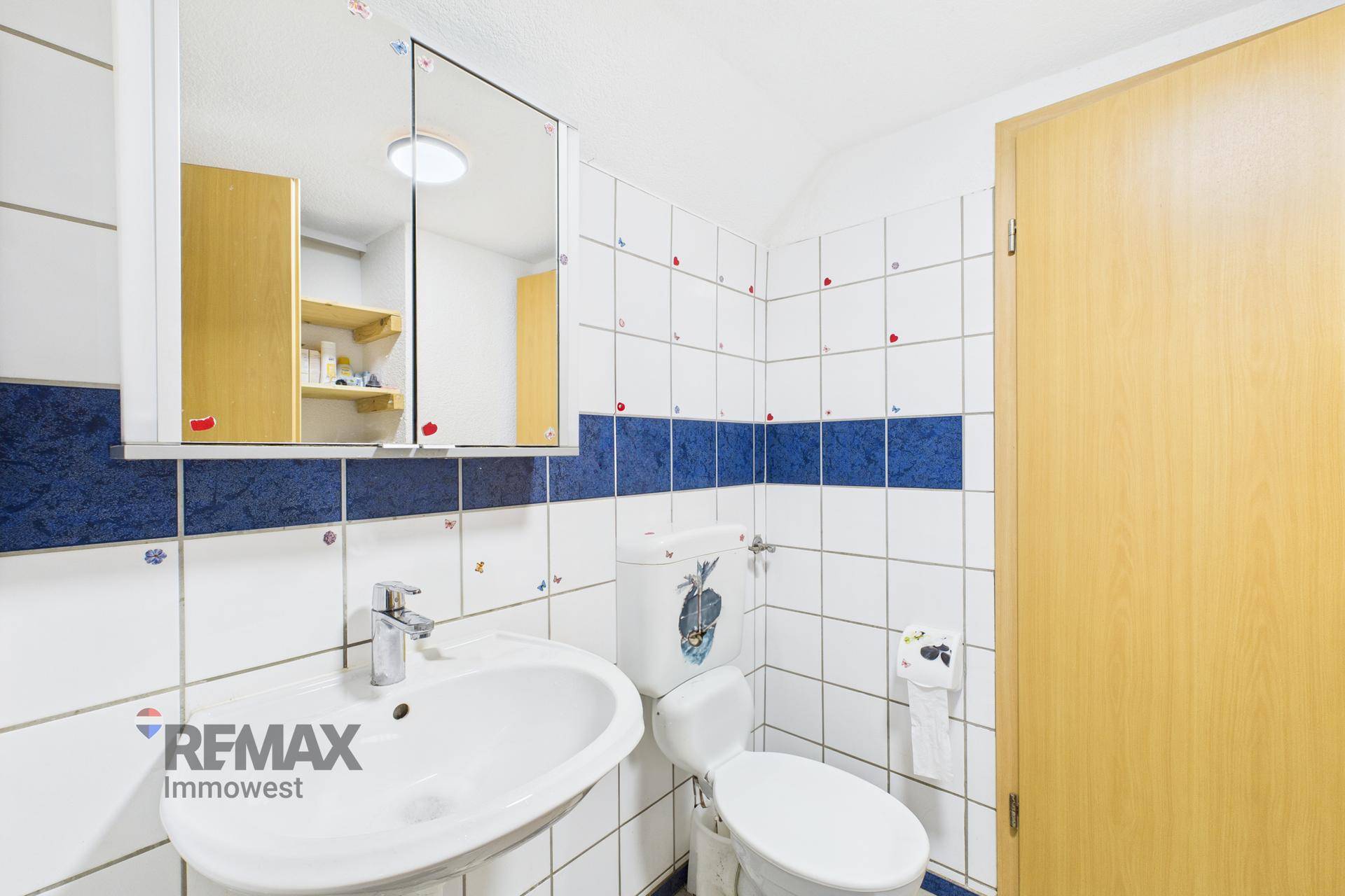 Badezimmer mit weiß-blauen Fliesen, Waschbecken und Toilette.