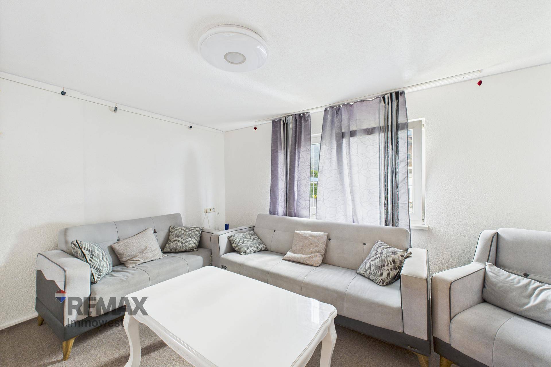 Gemütliches Wohnzimmer mit grauen Sofas, weißem Couchtisch und Teppichboden.