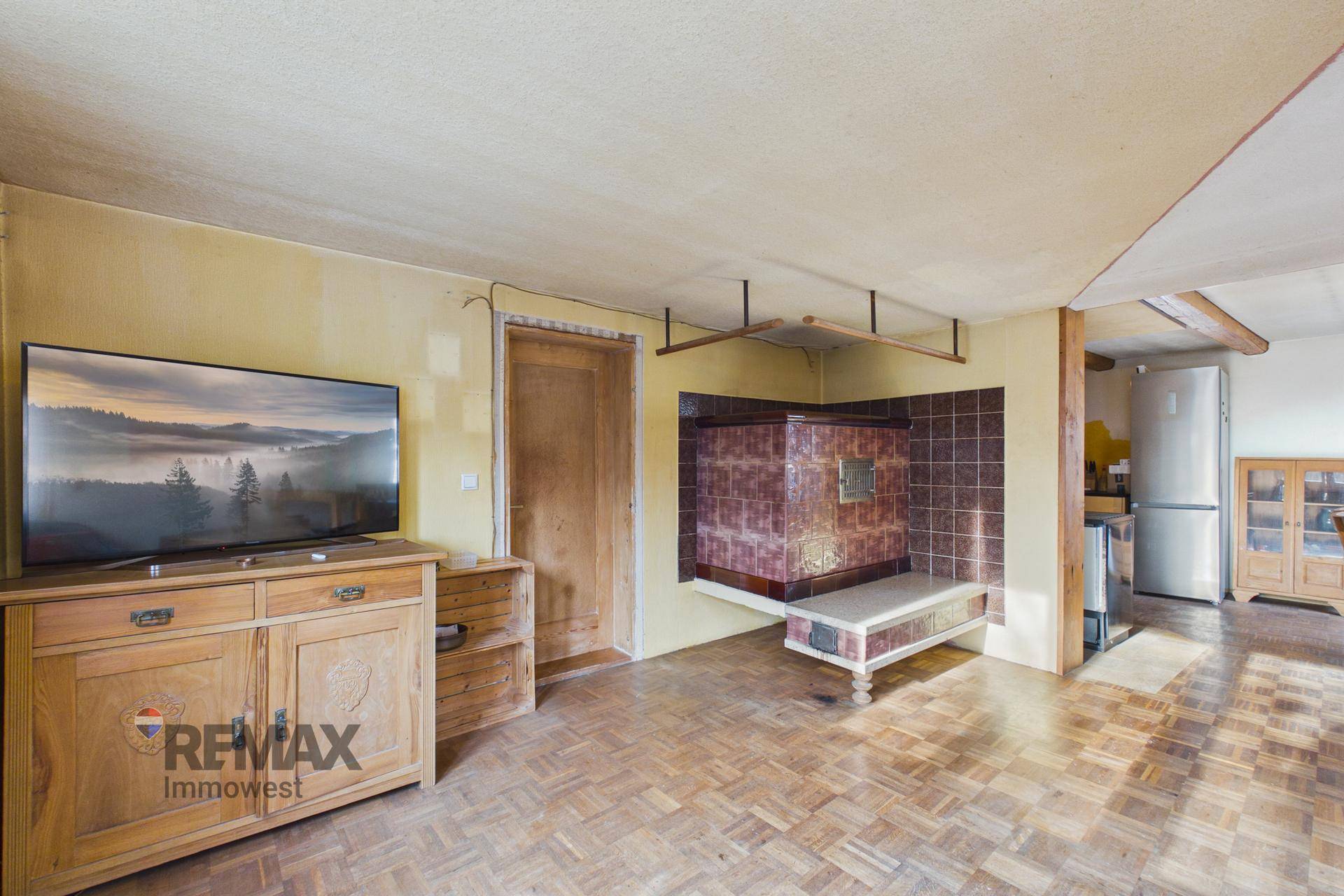 Gemütliches Wohnzimmer mit traditionellem Kachelofen, Holzboden und Fernseher.