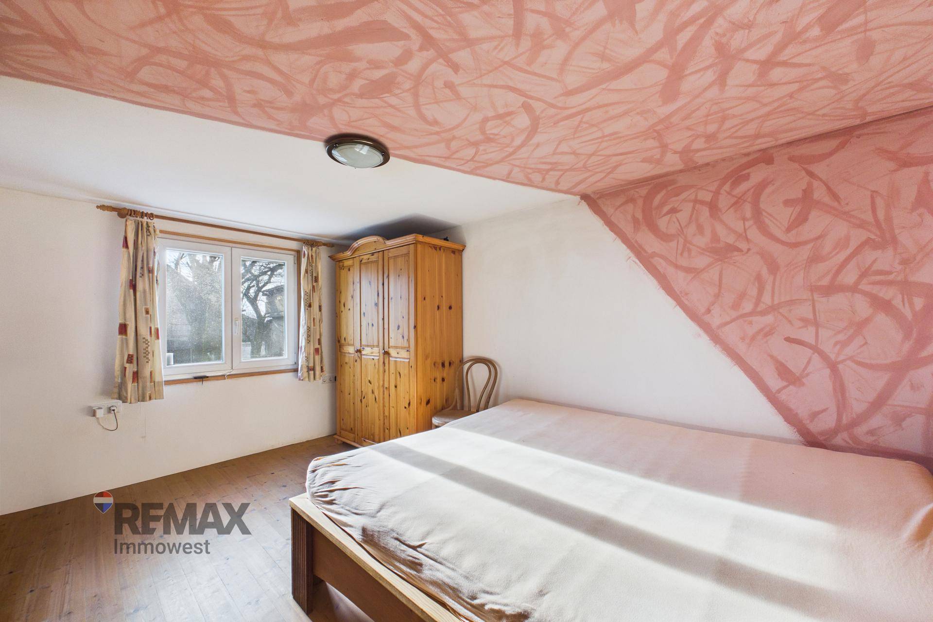 Helles Schlafzimmer mit Holzboden, Fenster und Blick ins Grüne.