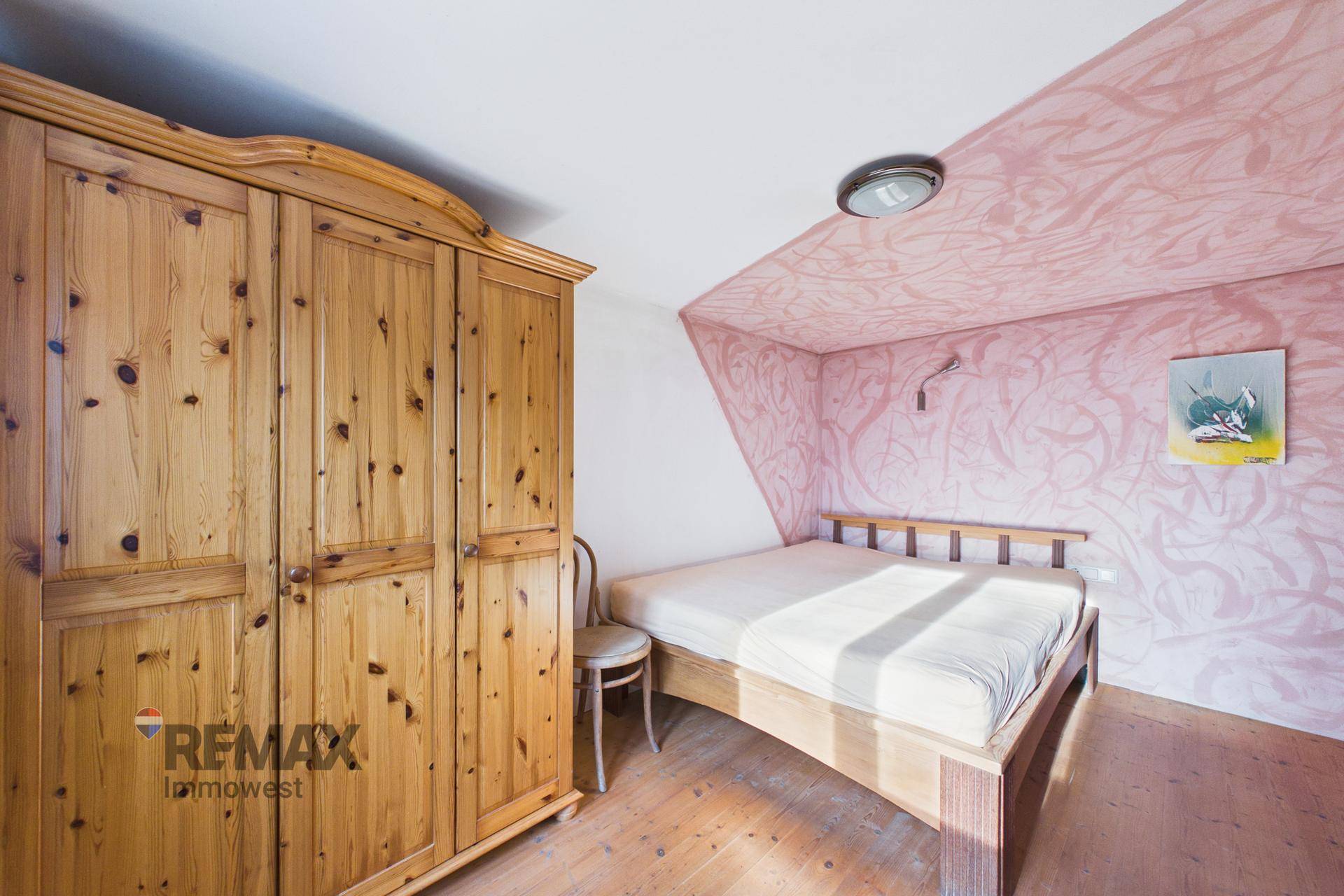 Schlafzimmer mit Holzbett, Kleiderschrank und dekorativer Wandgestaltung unter Dachschräge.