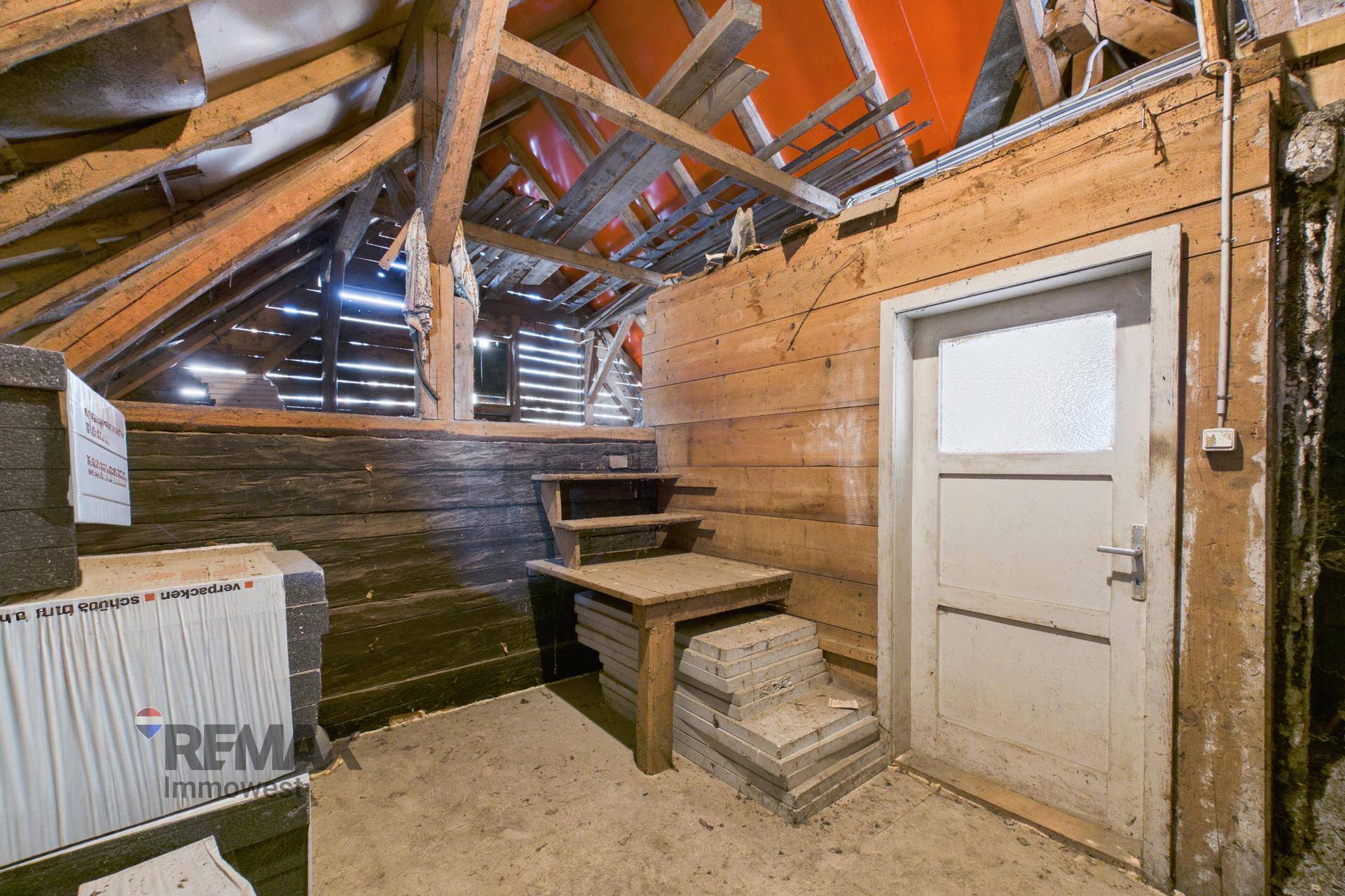 Teil des Dachbodens mit einer Holztür und einer kleinen Holztreppe, umgeben von Holzbalken.