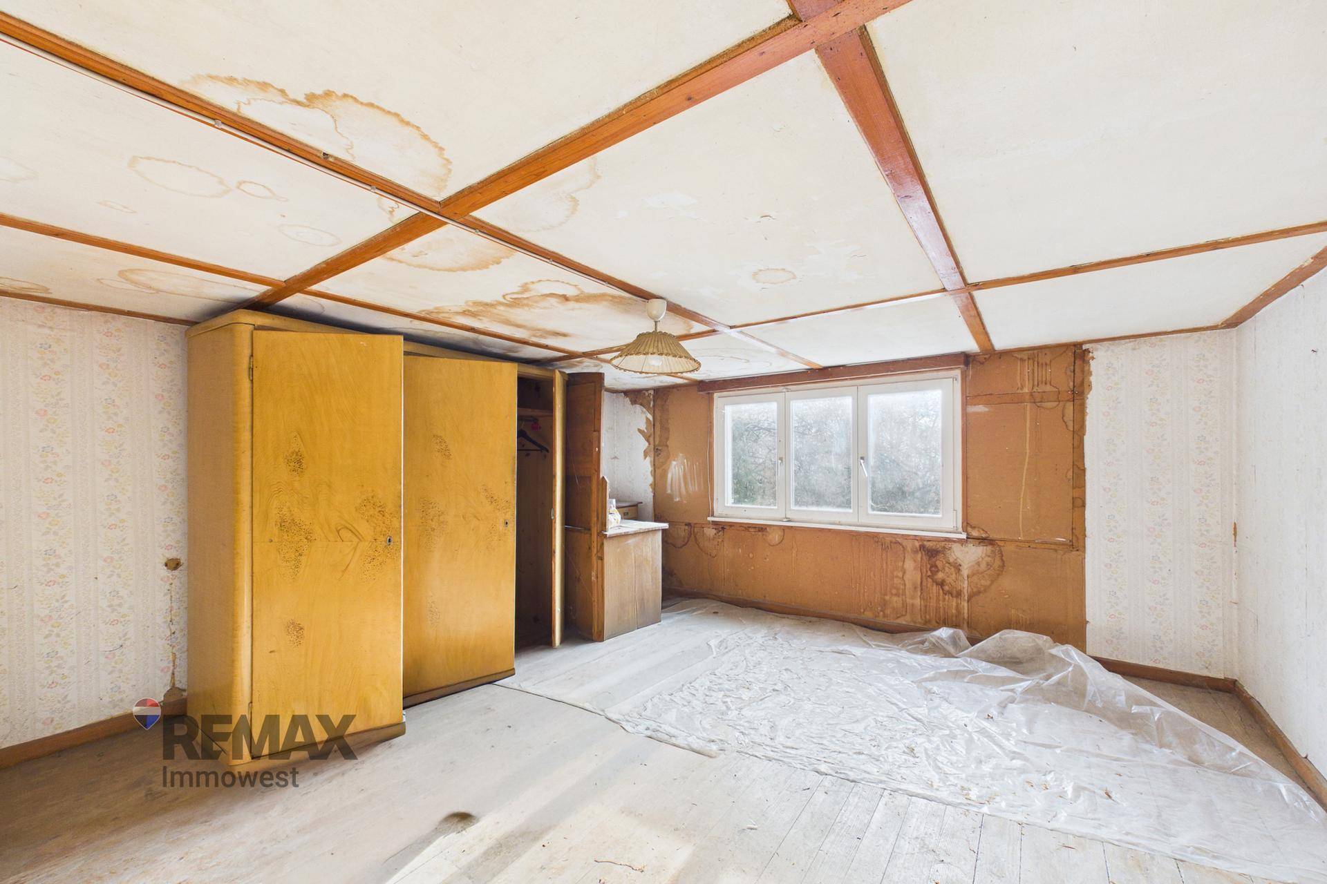 Weiteres Schlafzimmer mit sichtbaren Wasserschäden an der Decke und einem alten Holzschrank.