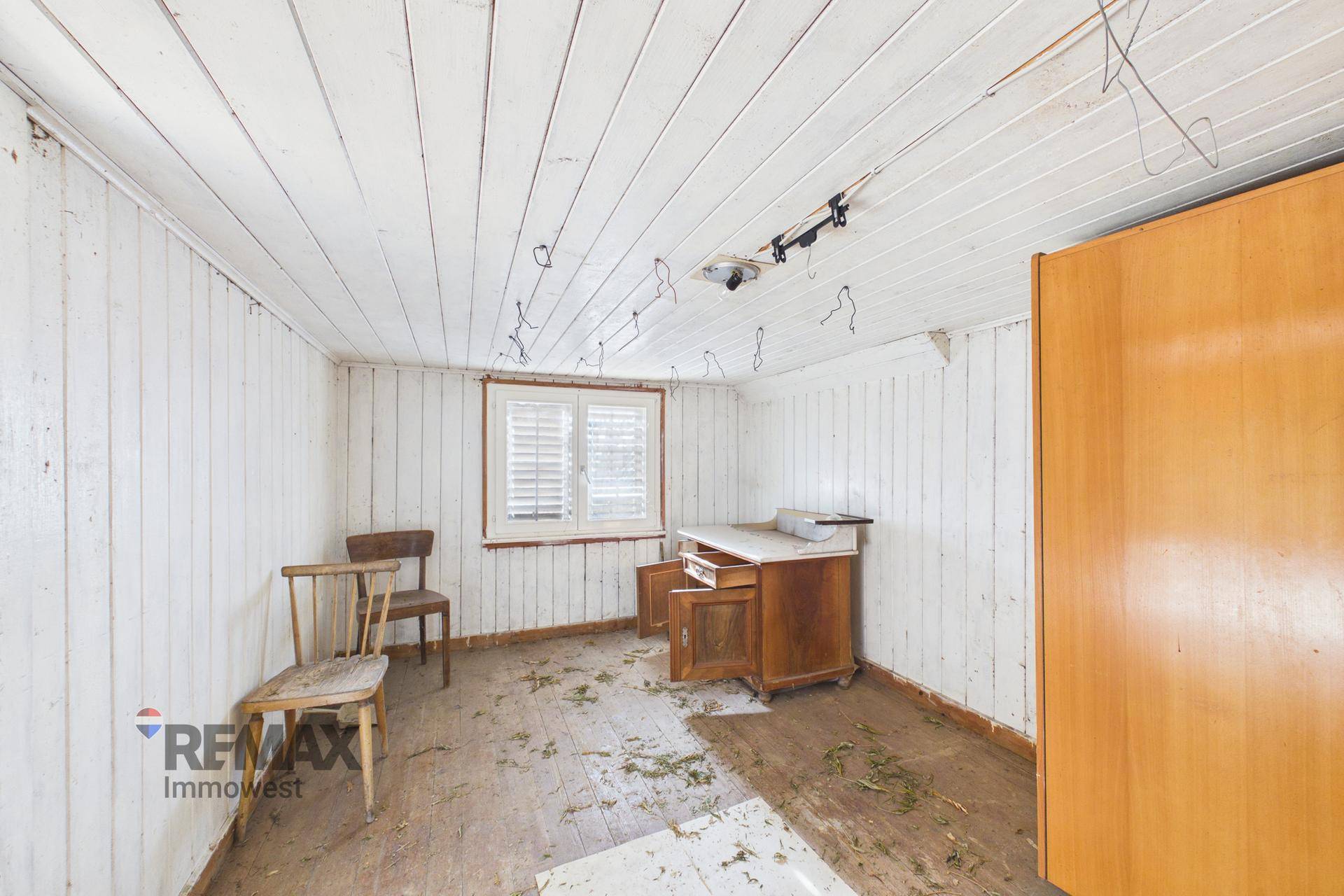 Zimmer mit weißer Holzverkleidung an Wänden und Decke, ausgestattet mit alten Holzmöbeln.