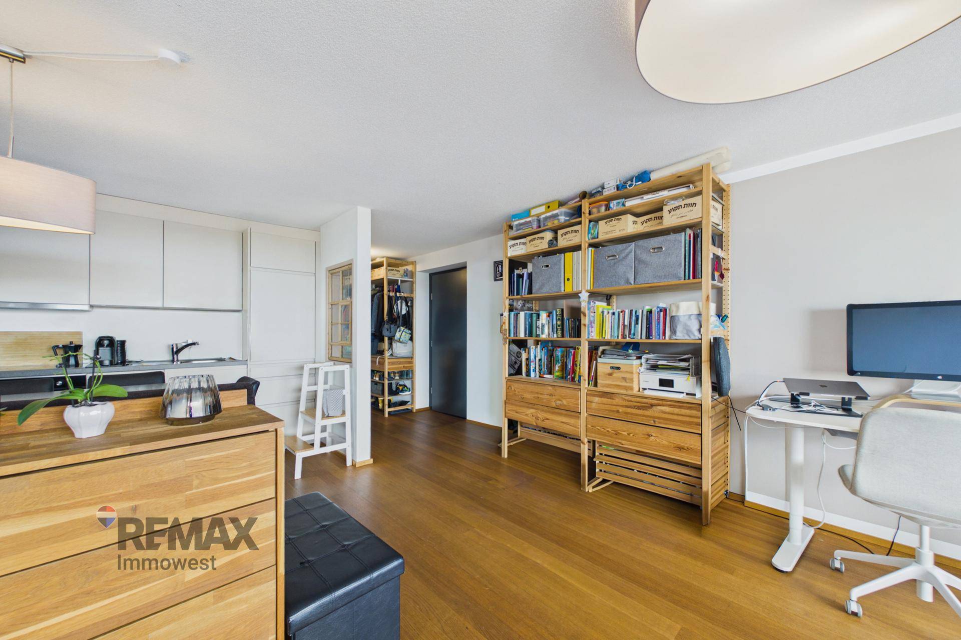 Offener Wohnbereich mit Holzboden, Bücherregal und einem Arbeitsplatz in heller Atmosphäre.