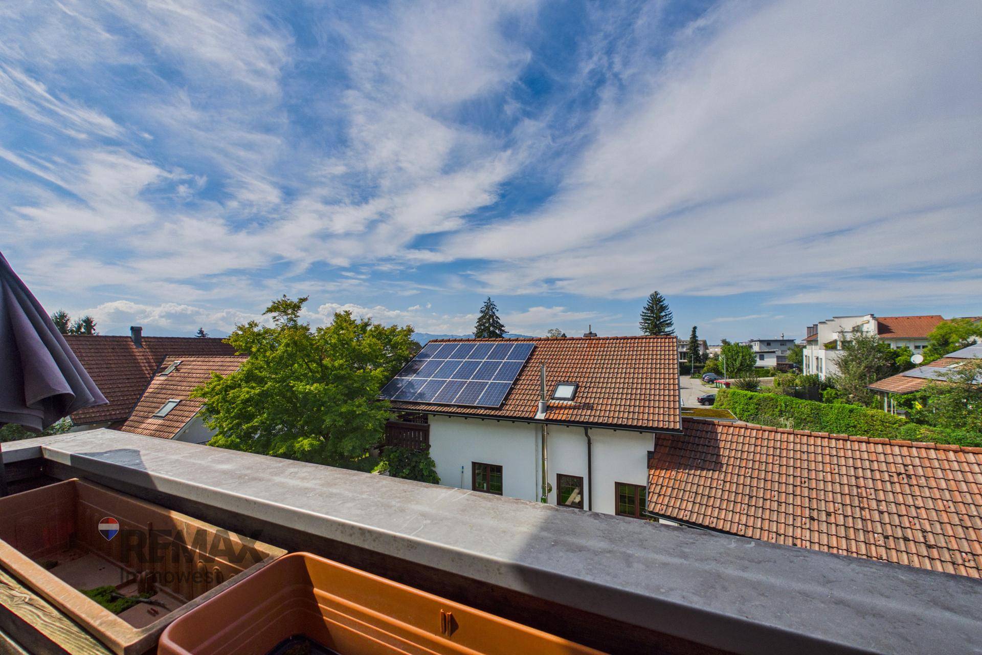 Weitblick vom Balkon über Dächer und grüne Umgebung unter blauem Himmel.