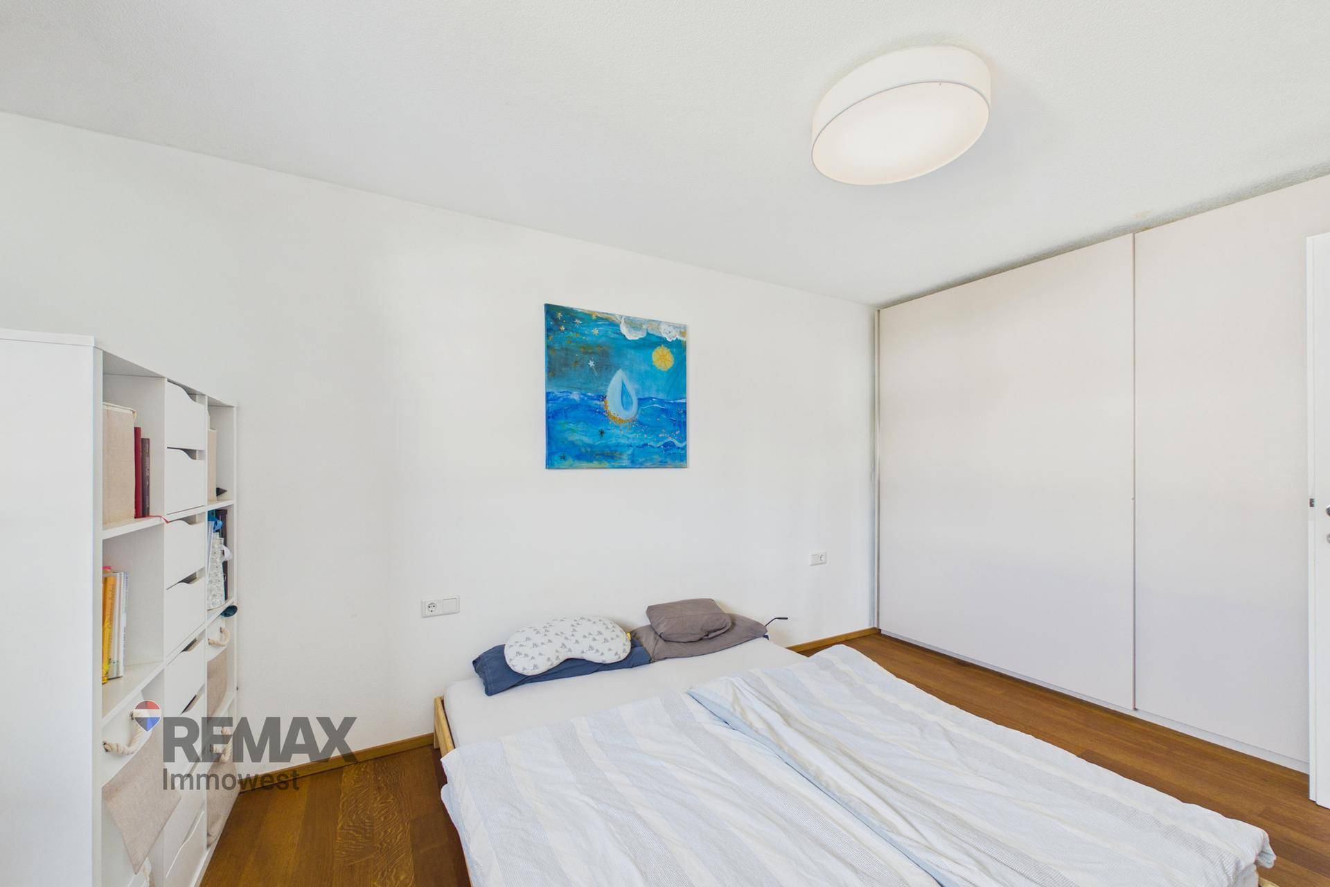 Schlafzimmer mit Holzboden, weißem Kleiderschrank und einem modernen Kunstwerk an der Wand.