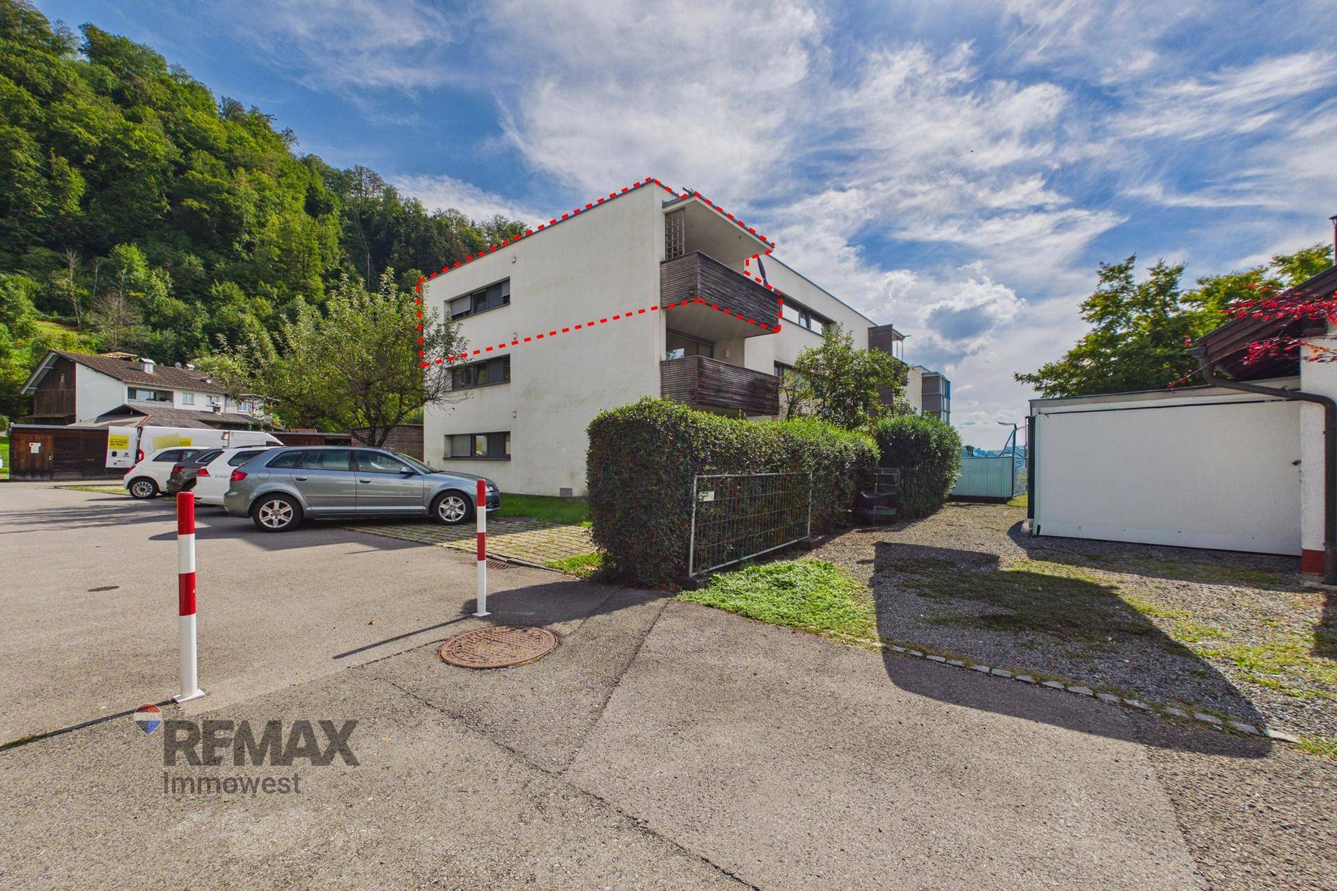 Mehrfamilienhaus mit Parkplätzen und grüner Umgebung, umgeben von Bäumen.