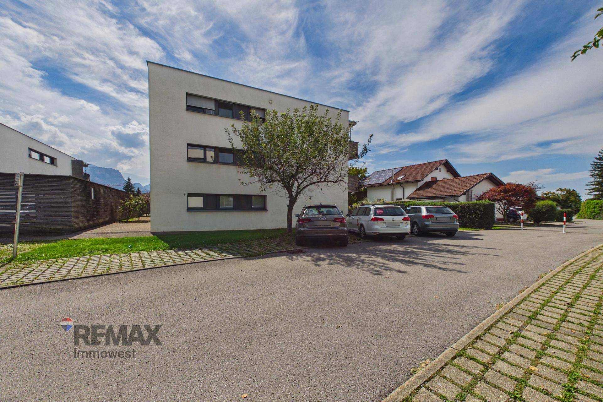 Modernes Wohngebäude mit Parkplätzen und gepflegter Außenanlage unter blauem Himmel.