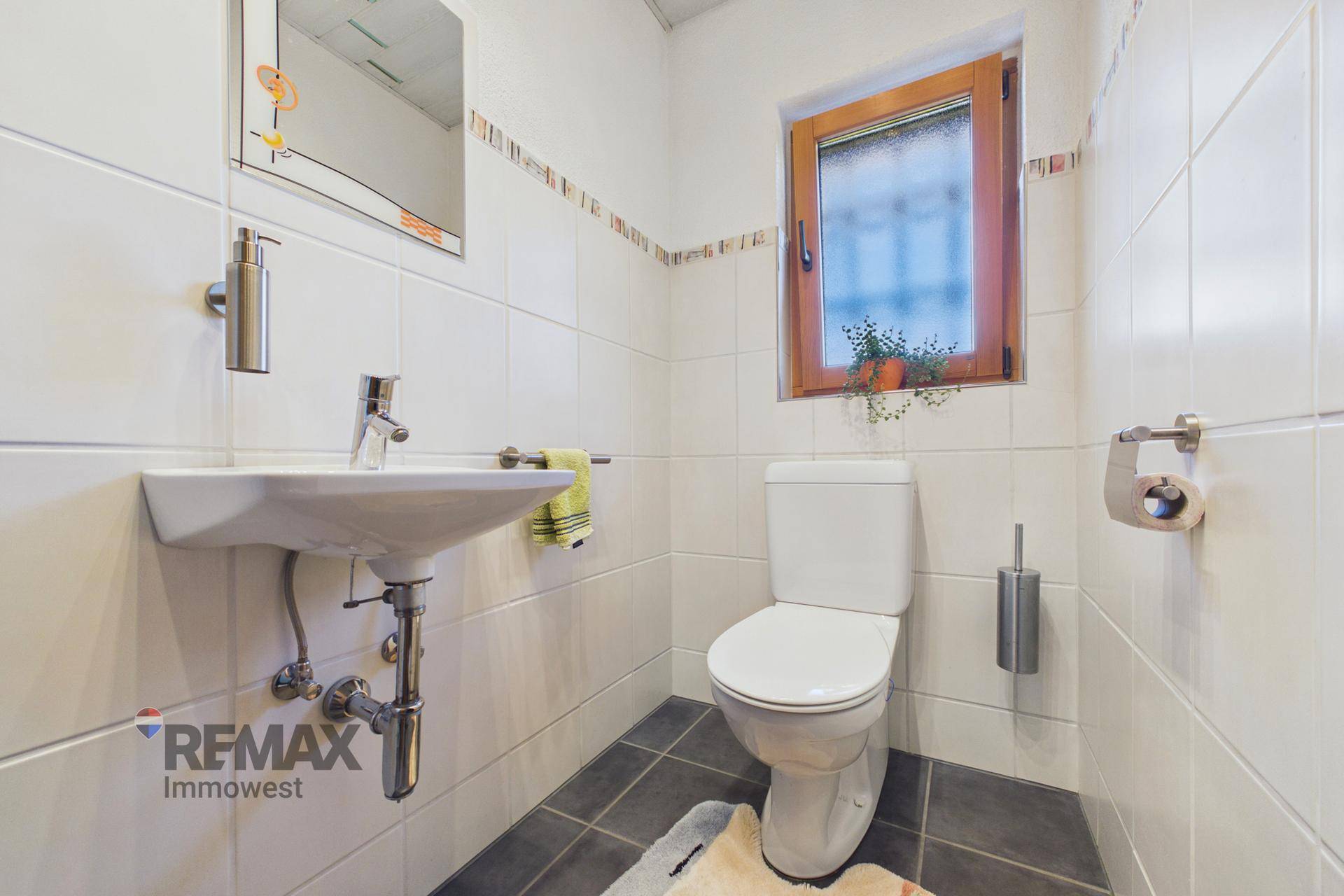 Kleines Gäste-WC mit Fenster, Waschbecken und hellen Fliesen.