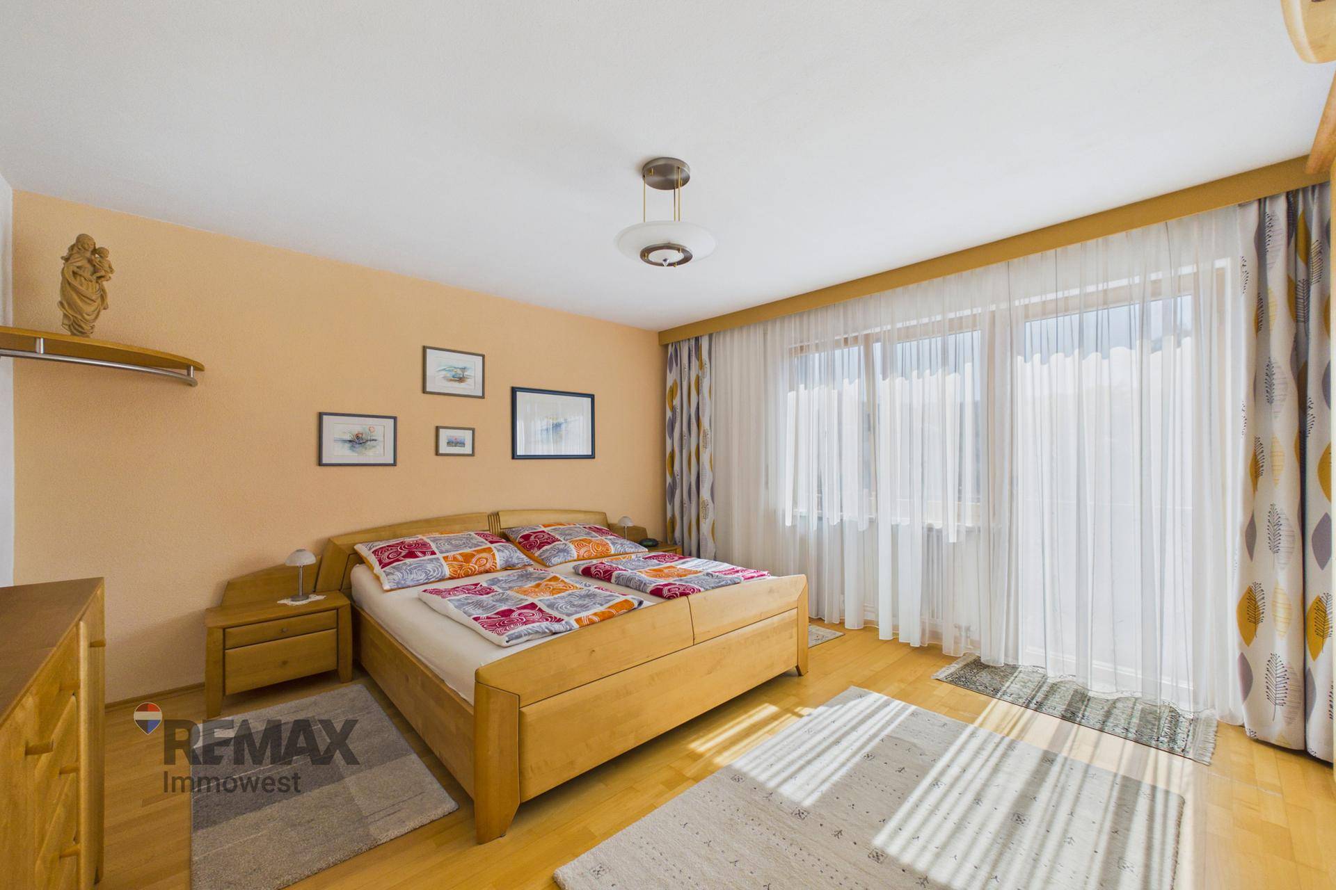 Geräumiges Schlafzimmer mit Doppelbett, Holzmöbeln und großen Fenstern.