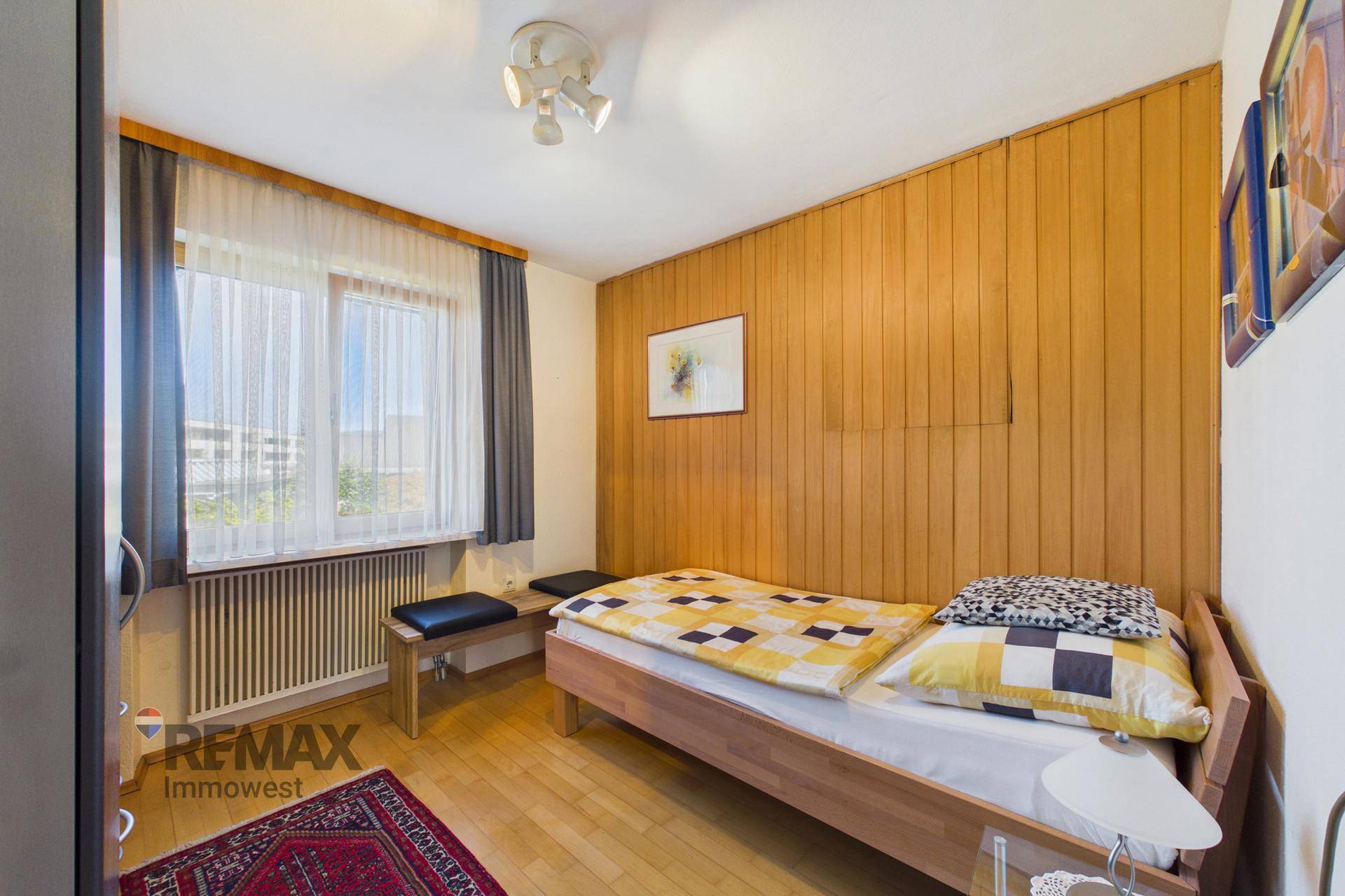 Gemütliches Schlafzimmer mit Einzelbett, Holzvertäfelung und Fensterblick.