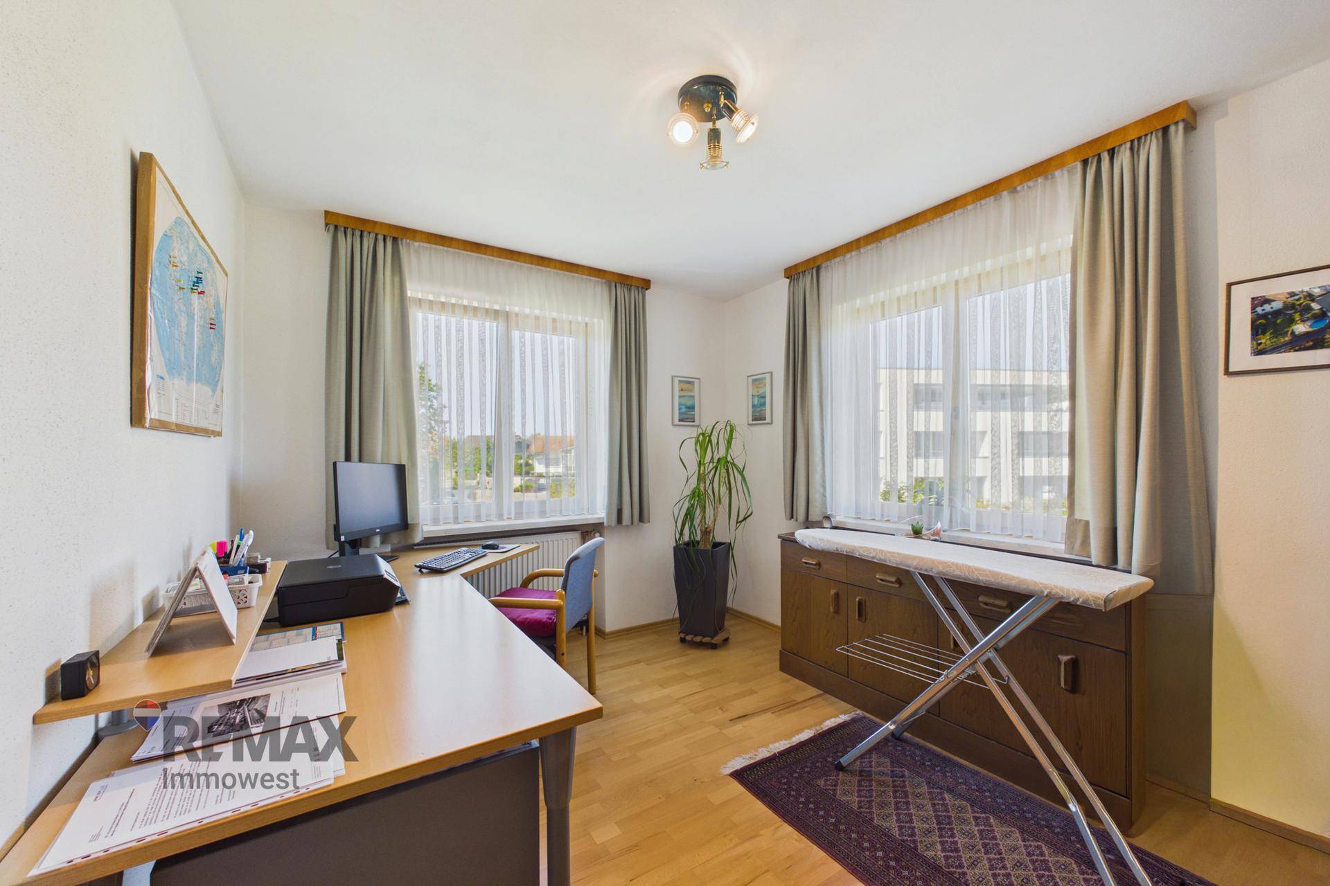 Helles Arbeitszimmer mit zwei Fenstern, Schreibtisch und Parkettboden.