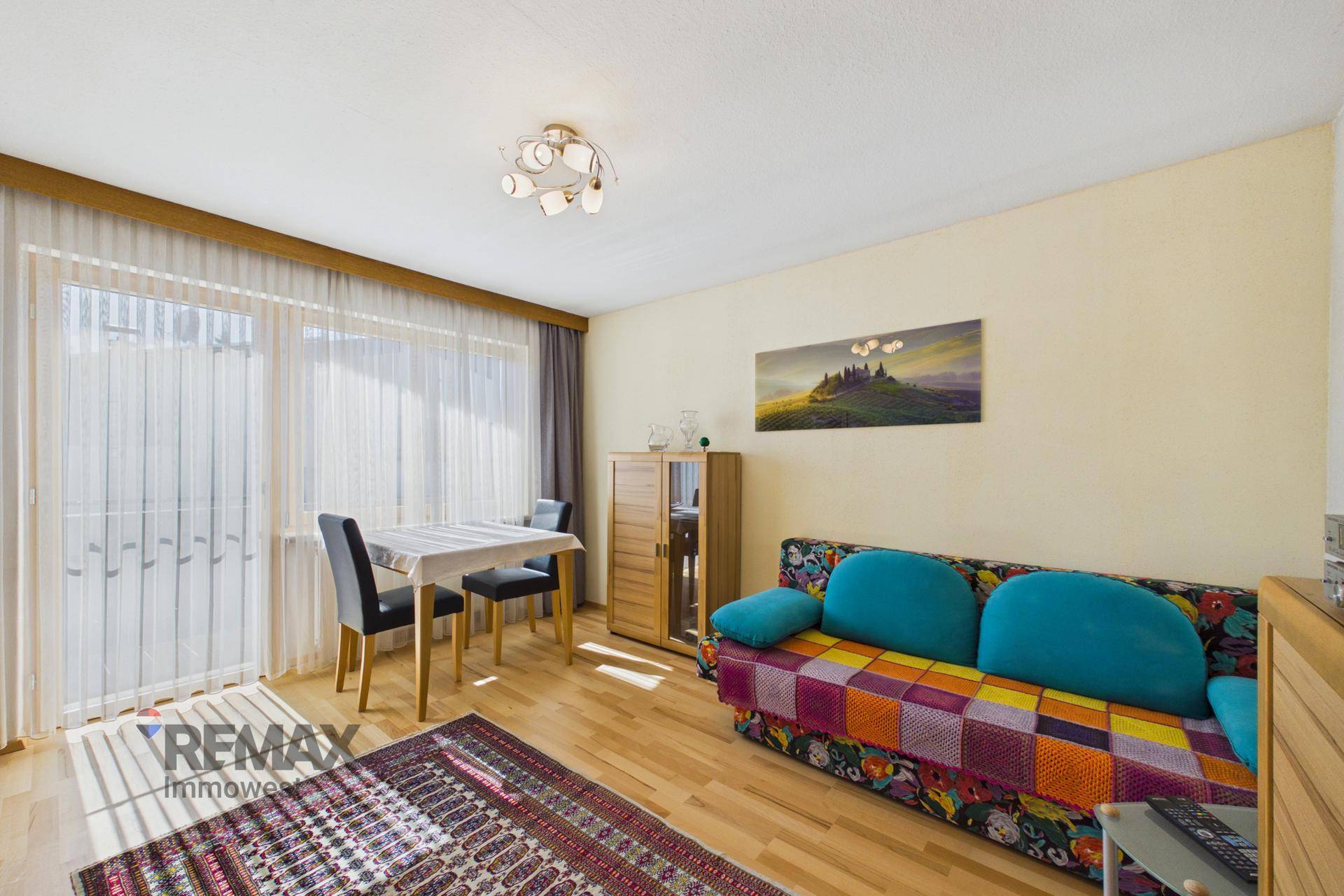 Freundliches Zimmer mit Schlafsofa, Esstisch und Zugang zum Balkon.