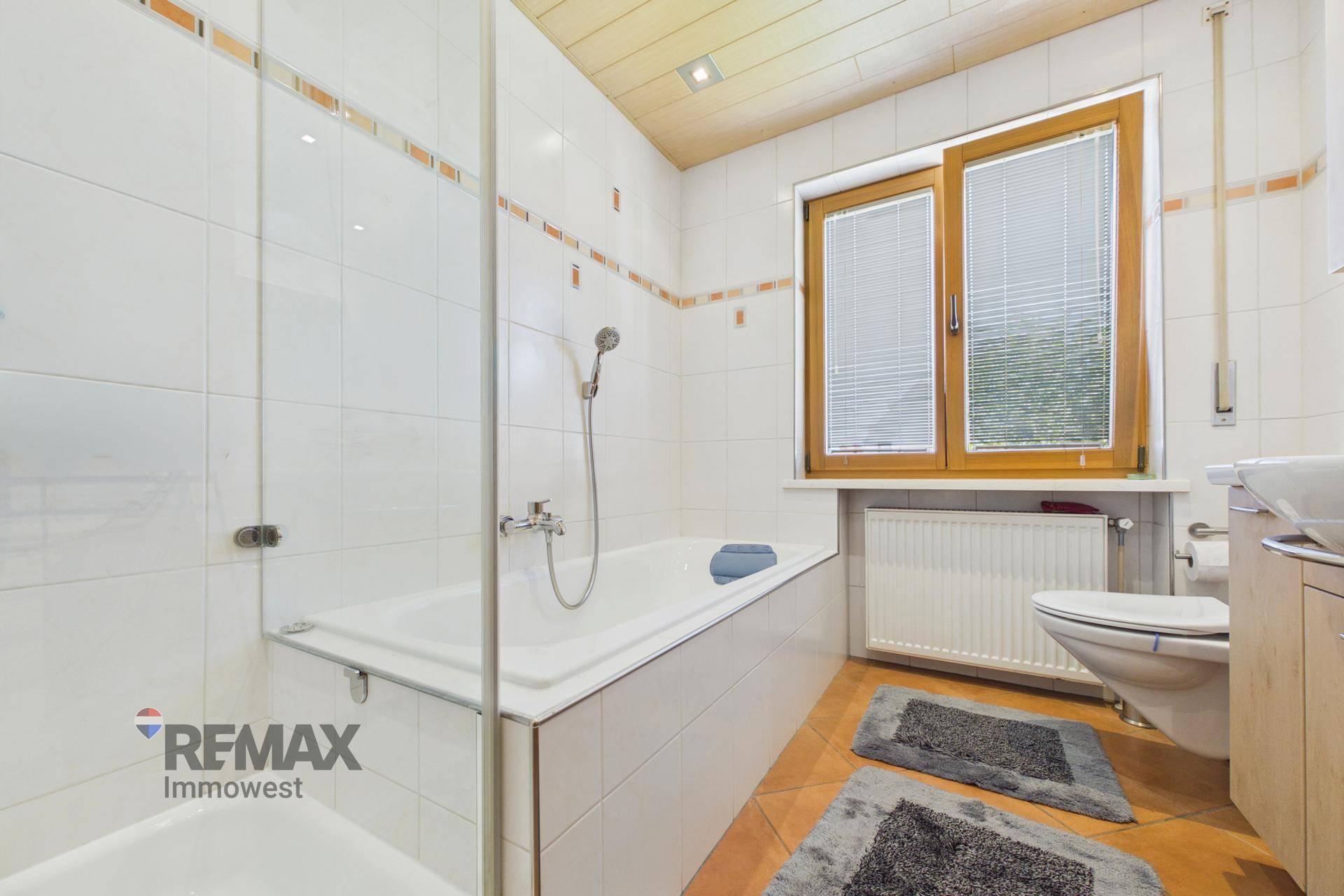 Helles Badezimmer mit Badewanne, Dusche, WC und Fenster.