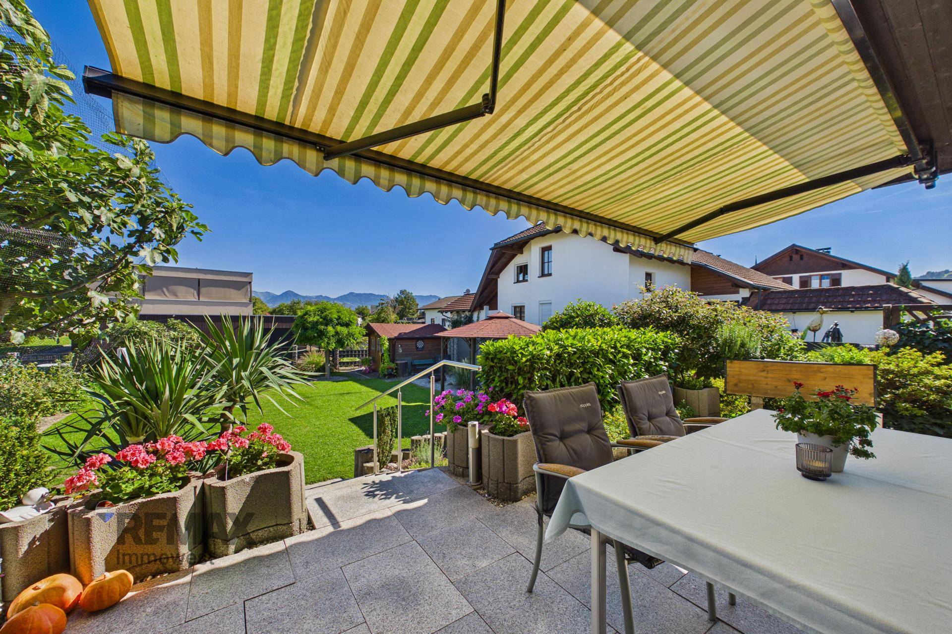 Gemütliche Terrasse mit Markise, Gartenmöbeln und Blick ins Grüne an einem sonnigen Tag.