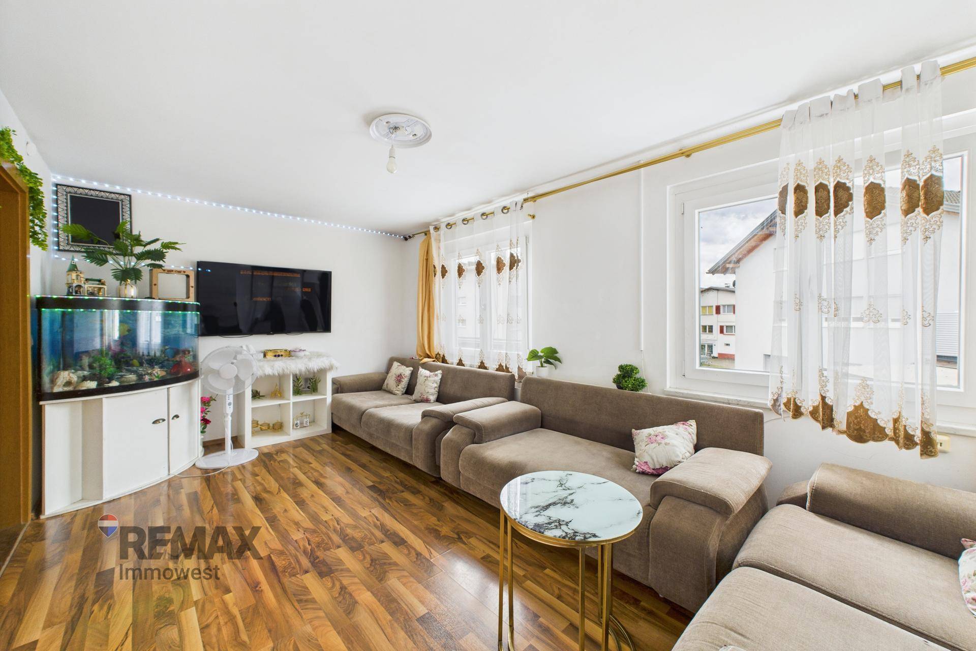 Gemütliches Wohnzimmer mit großem Sofa, Fernseher, Aquarium und Holzboden.