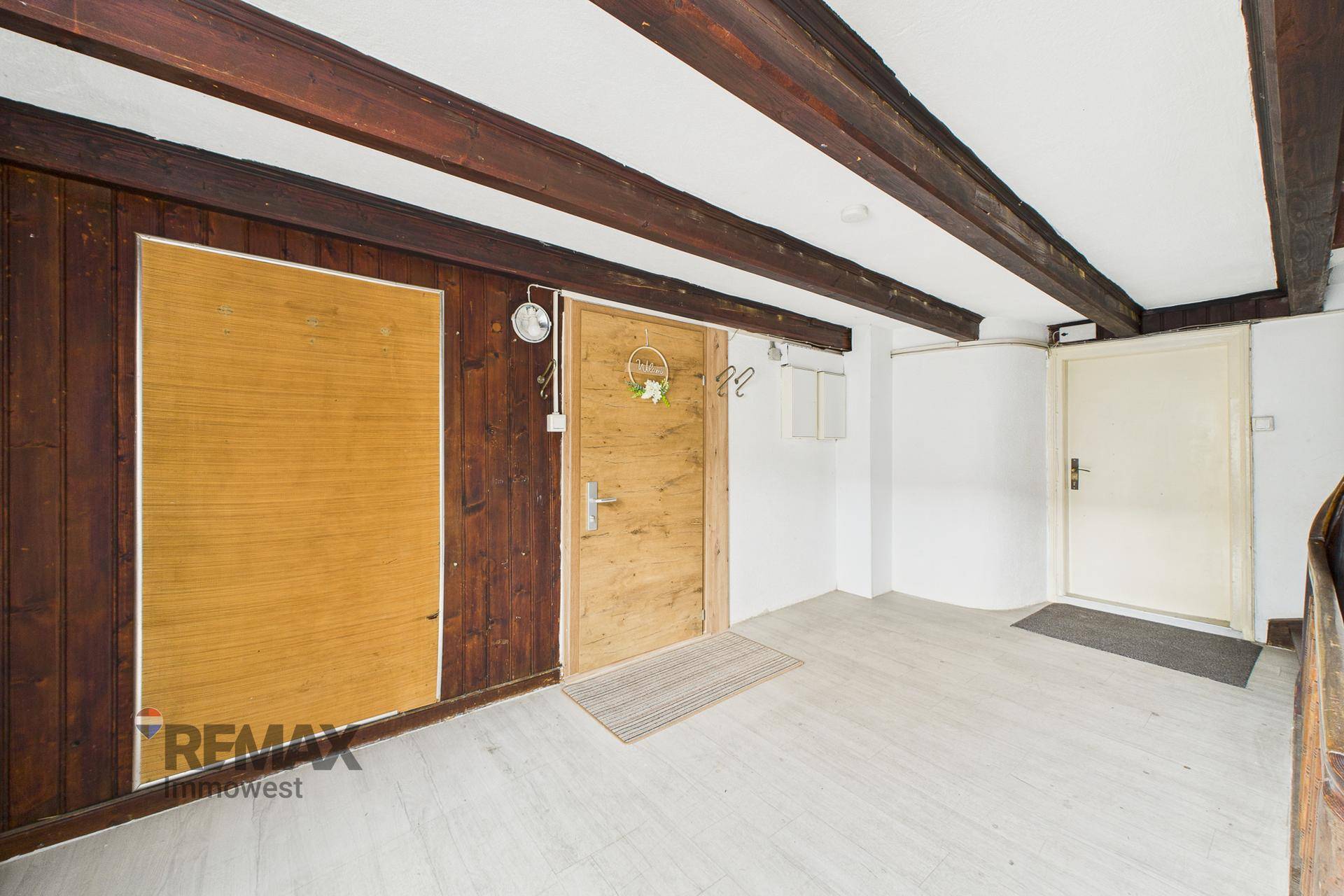 Eingangsbereich mit Holzbalken an der Decke und zwei Holztüren.