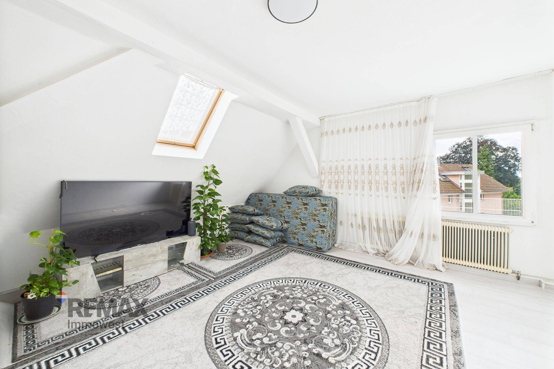 Helles Wohnzimmer im Dachgeschoss mit Teppichboden, Fernseher und Dachfenster.
