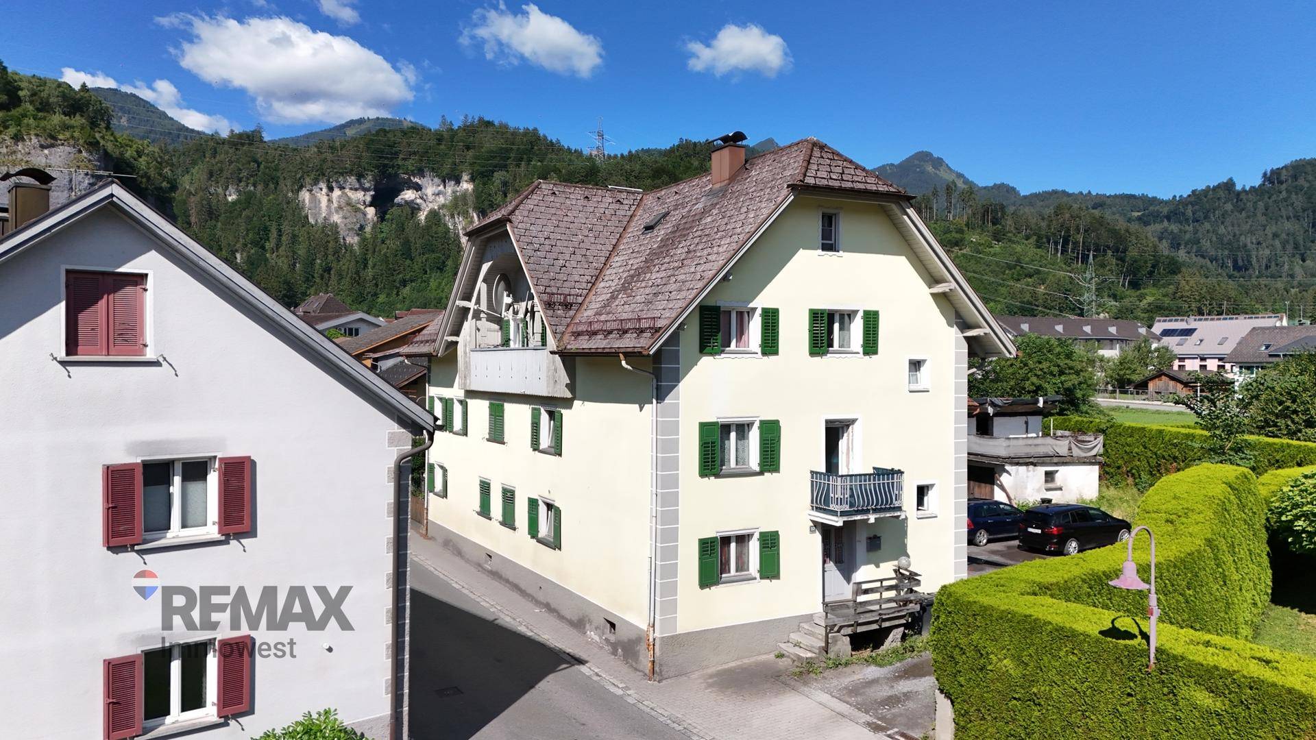Traditionelles Haus mit grünen Fensterläden und Balkon vor alpiner Bergkulisse.