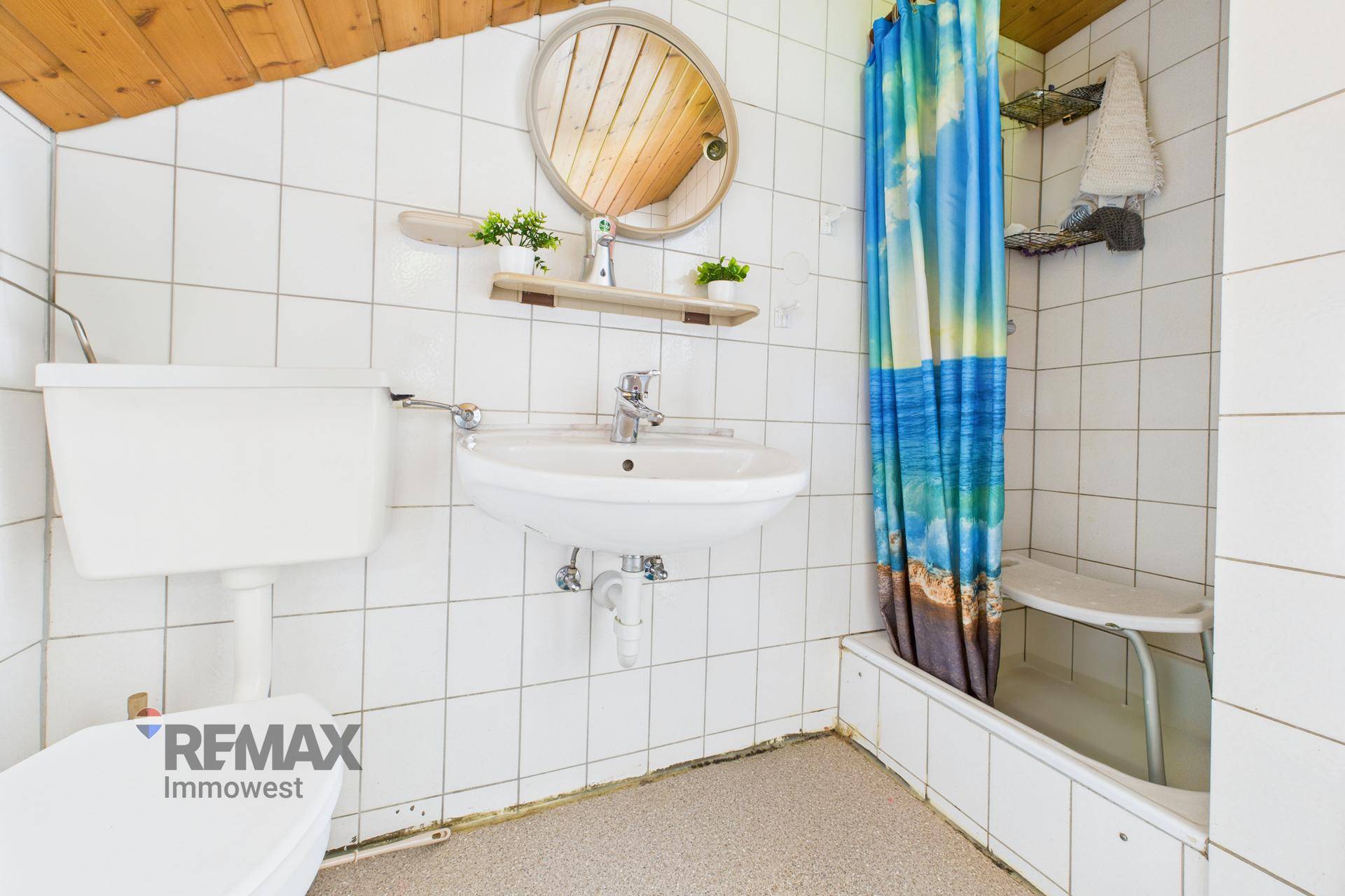 Badezimmer mit weißen Fliesen, Waschbecken, Toilette und Duschbereich im 80er-Jahre-Stil.
