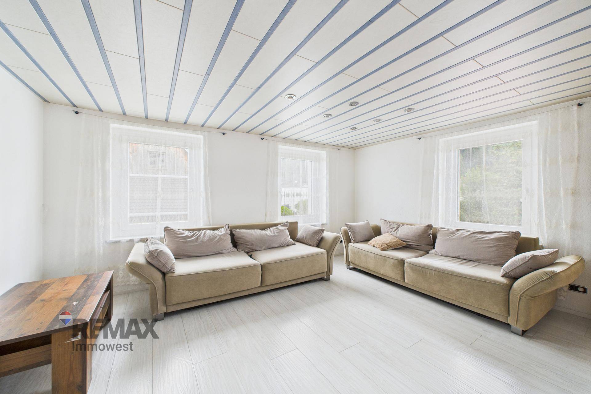 Helles Wohnzimmer mit zwei Sofas, Holzboden und dekorativer Deckenverkleidung.