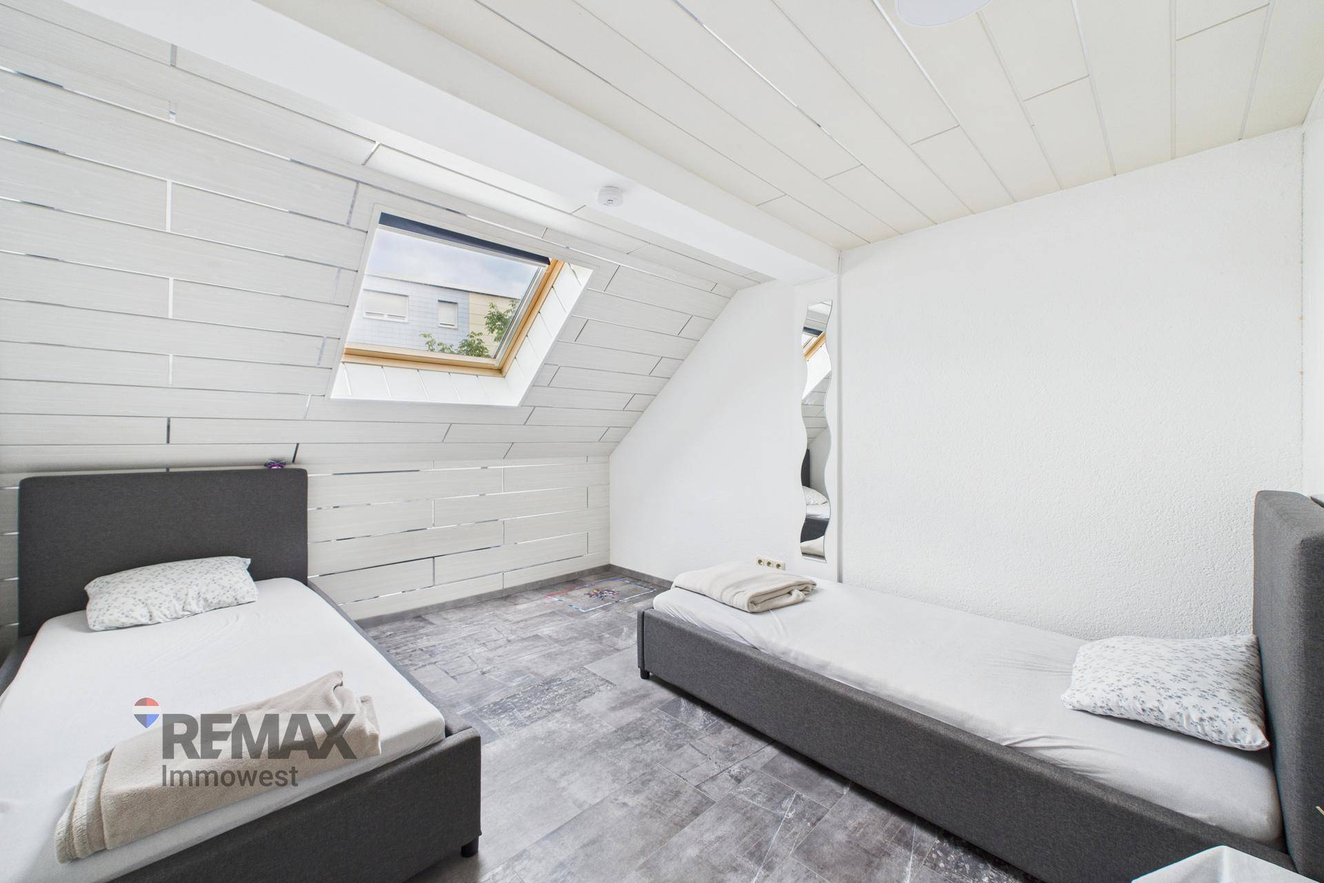 Dachgeschoss-Schlafzimmer mit zwei Einzelbetten, Dachfenster und Holzverkleidung.