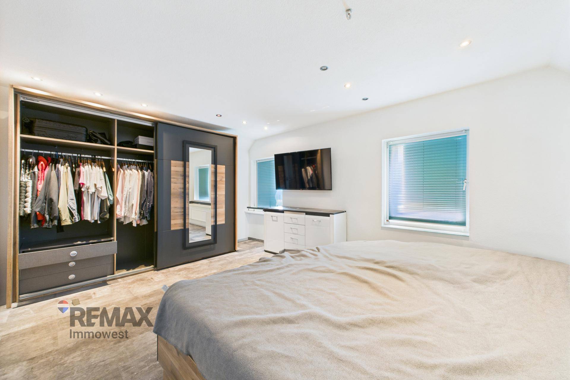 Helles Schlafzimmer mit großem Bett, Einbauschrank und Fernseher an der Wand.