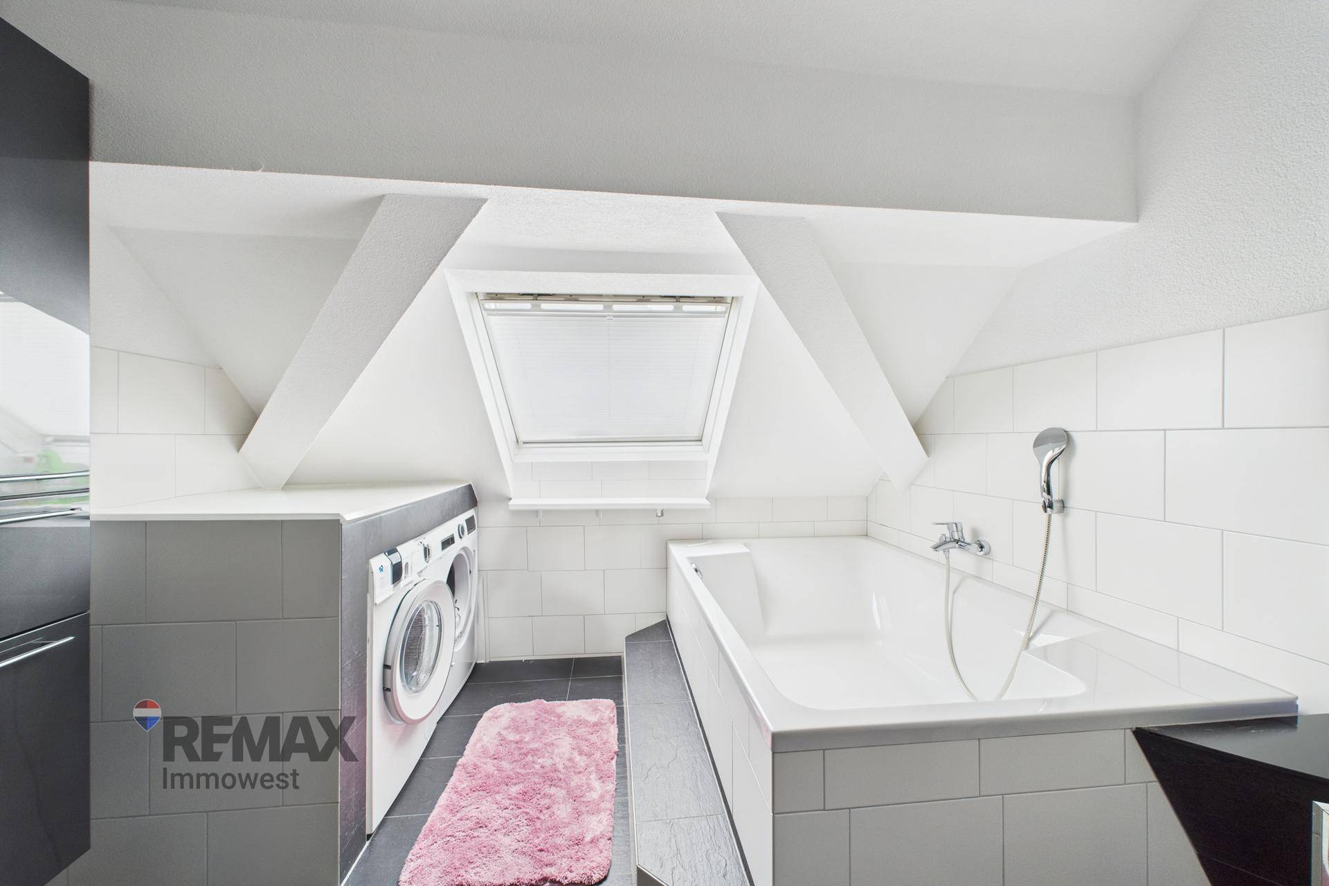Badezimmer im Dachgeschoss mit Badewanne, Waschmaschine und Dachfenster für Tageslicht.