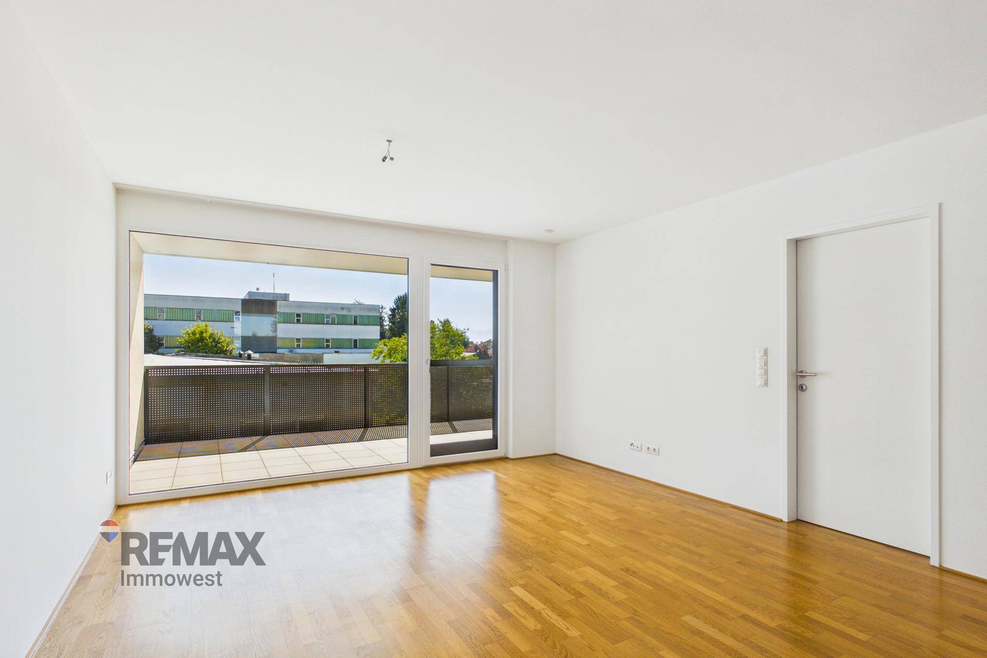 Heller Wohnraum mit Holzboden und großen Glasfronten, die Zugang zu einem Außenbereich bieten.