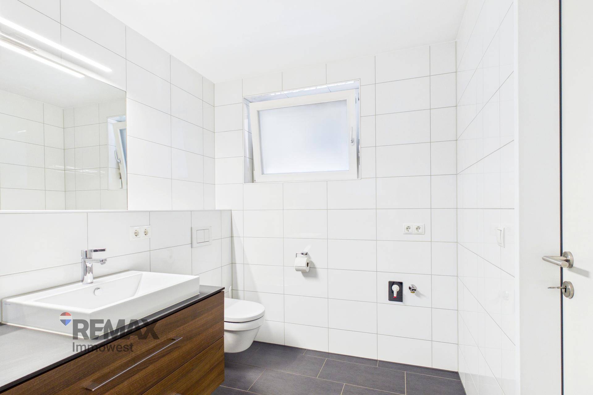 Helles Badezimmer mit Fenster, modernen Fliesen, Waschtisch und wandhängendem WC.