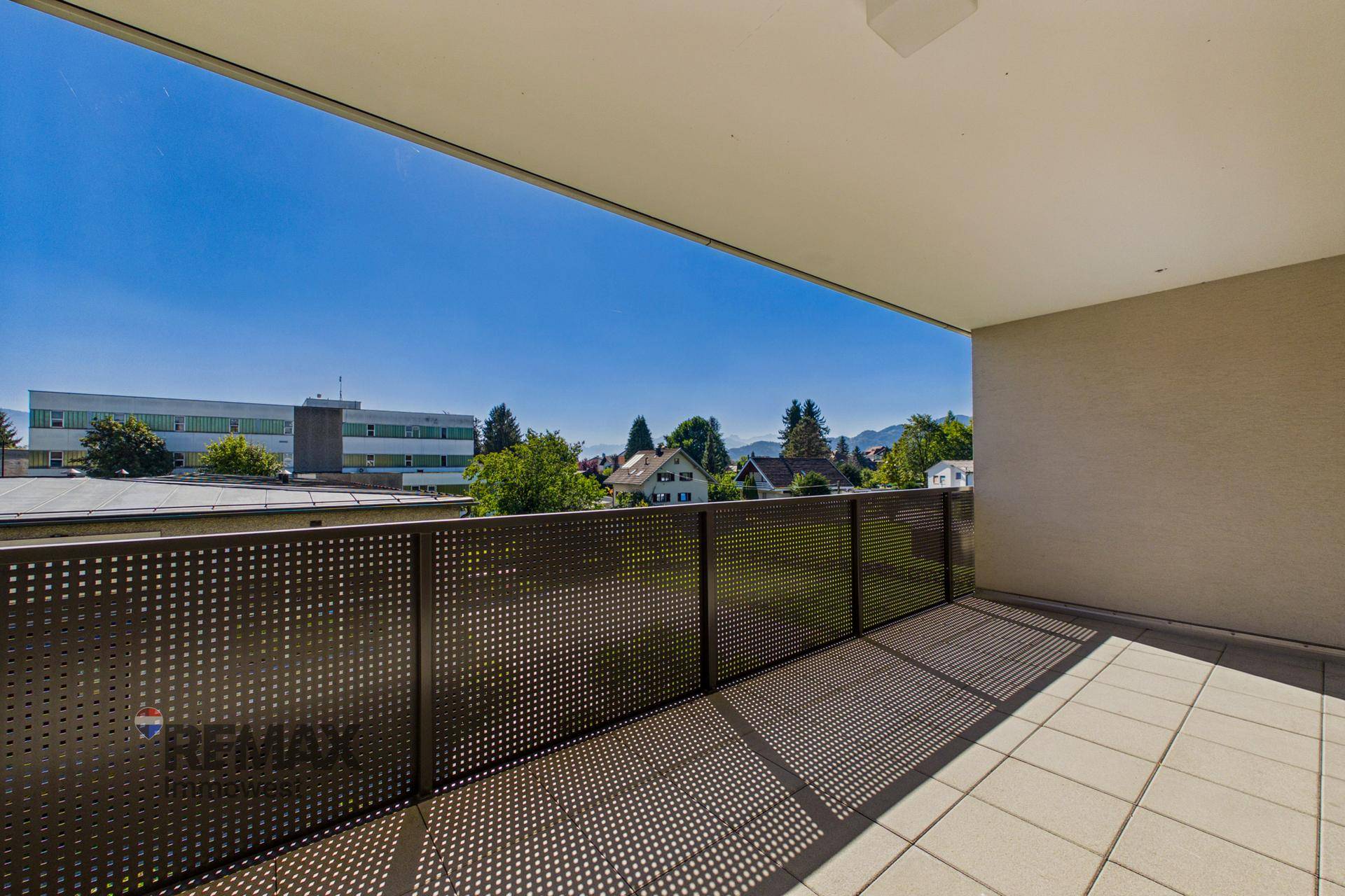 Geräumiger Balkon mit Fliesenboden und Metallgeländer, bietet einen weiten Blick auf die Umgebung und Berge.