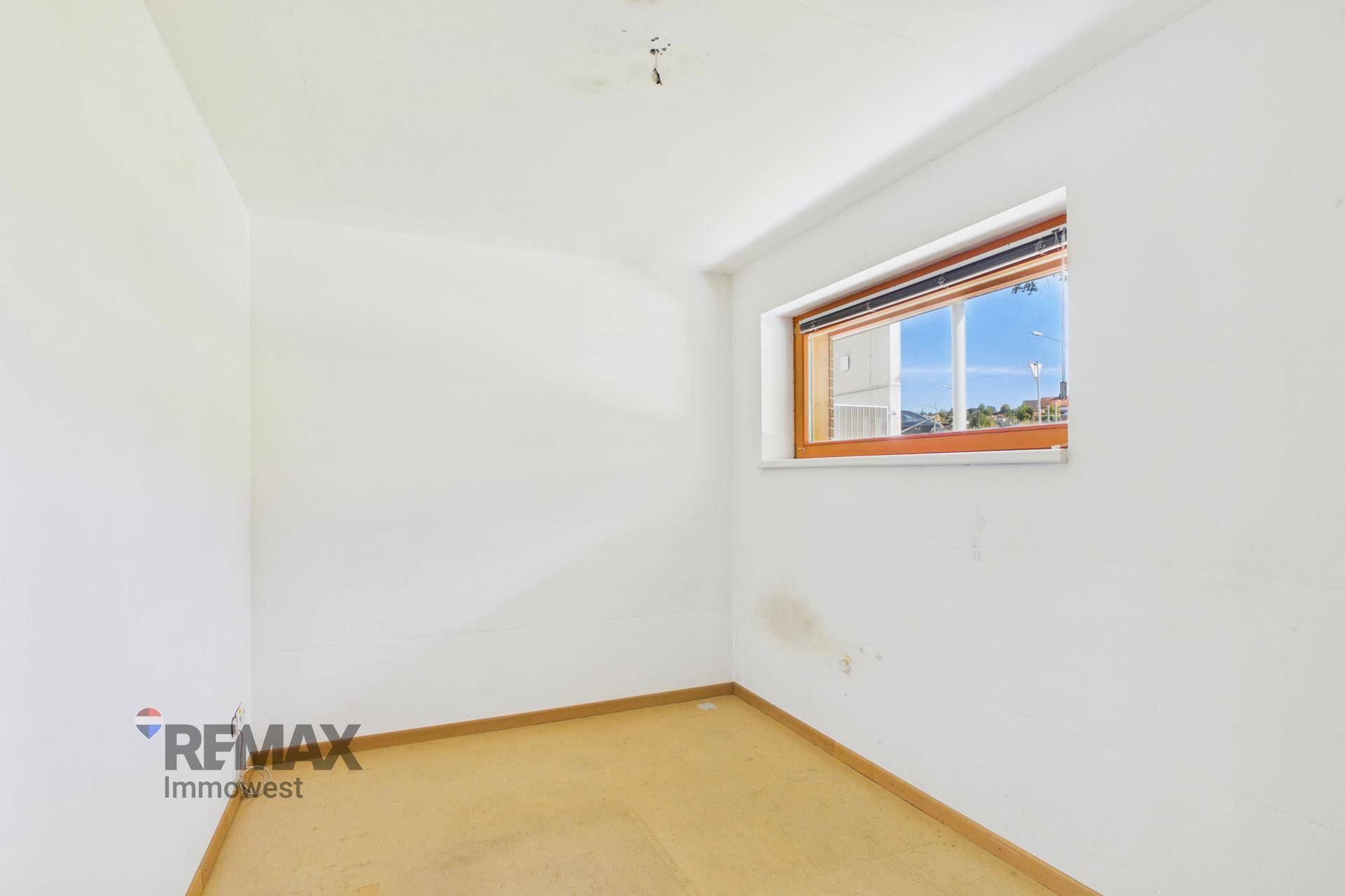 Kleines, helles Zimmer mit weiß gestrichenen Wänden und einem Fenster.