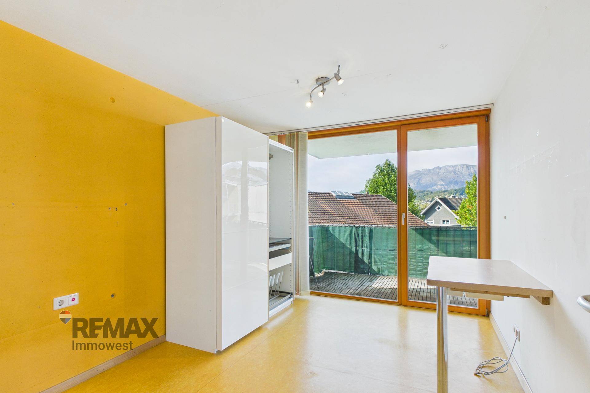 Helles Schlafzimmer mit gelber Wand, weißem Schrank und Balkonzugang mit Bergblick.