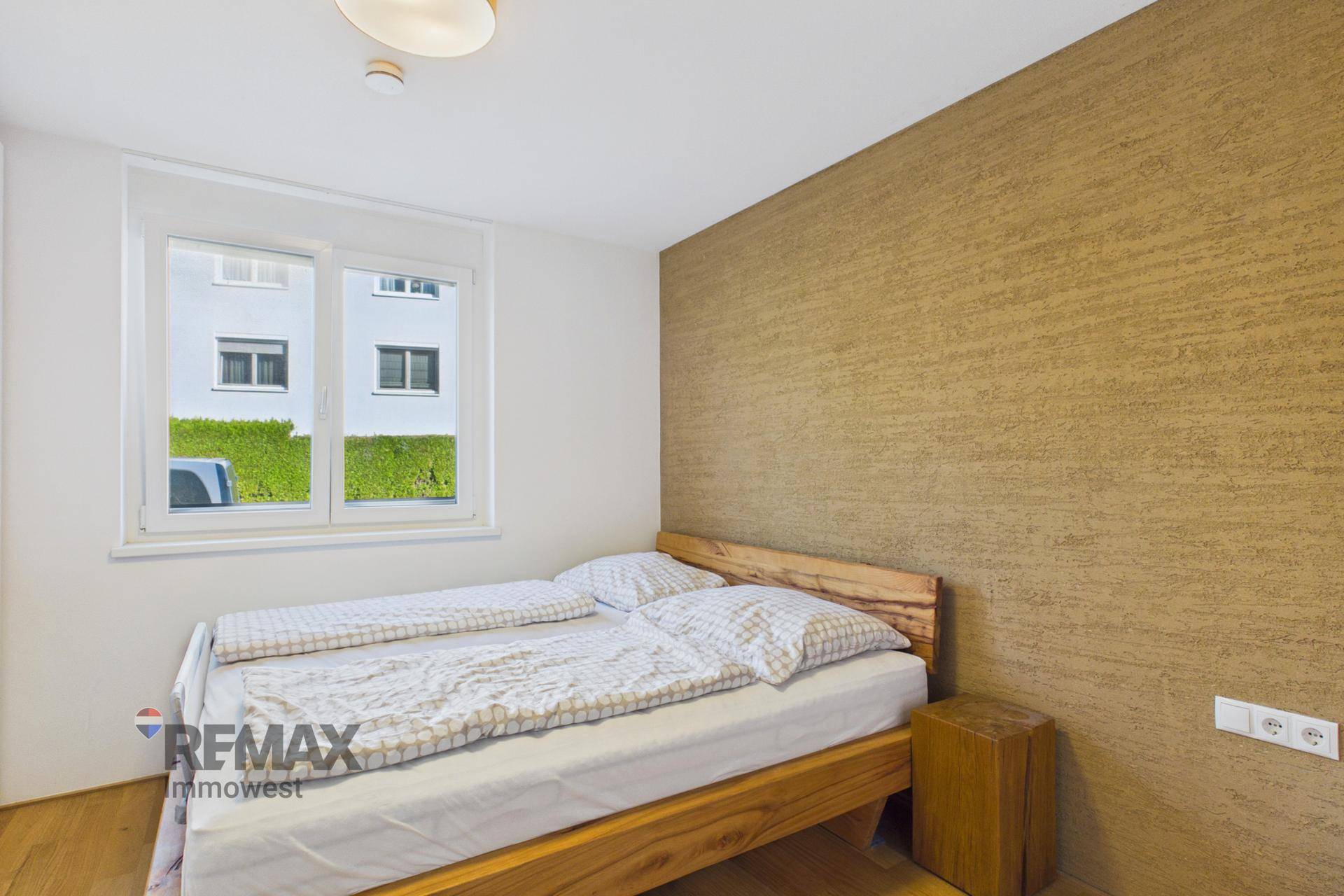 Schlafzimmer mit Holzbett, Holzboden und einer strukturierten Akzentwand.
