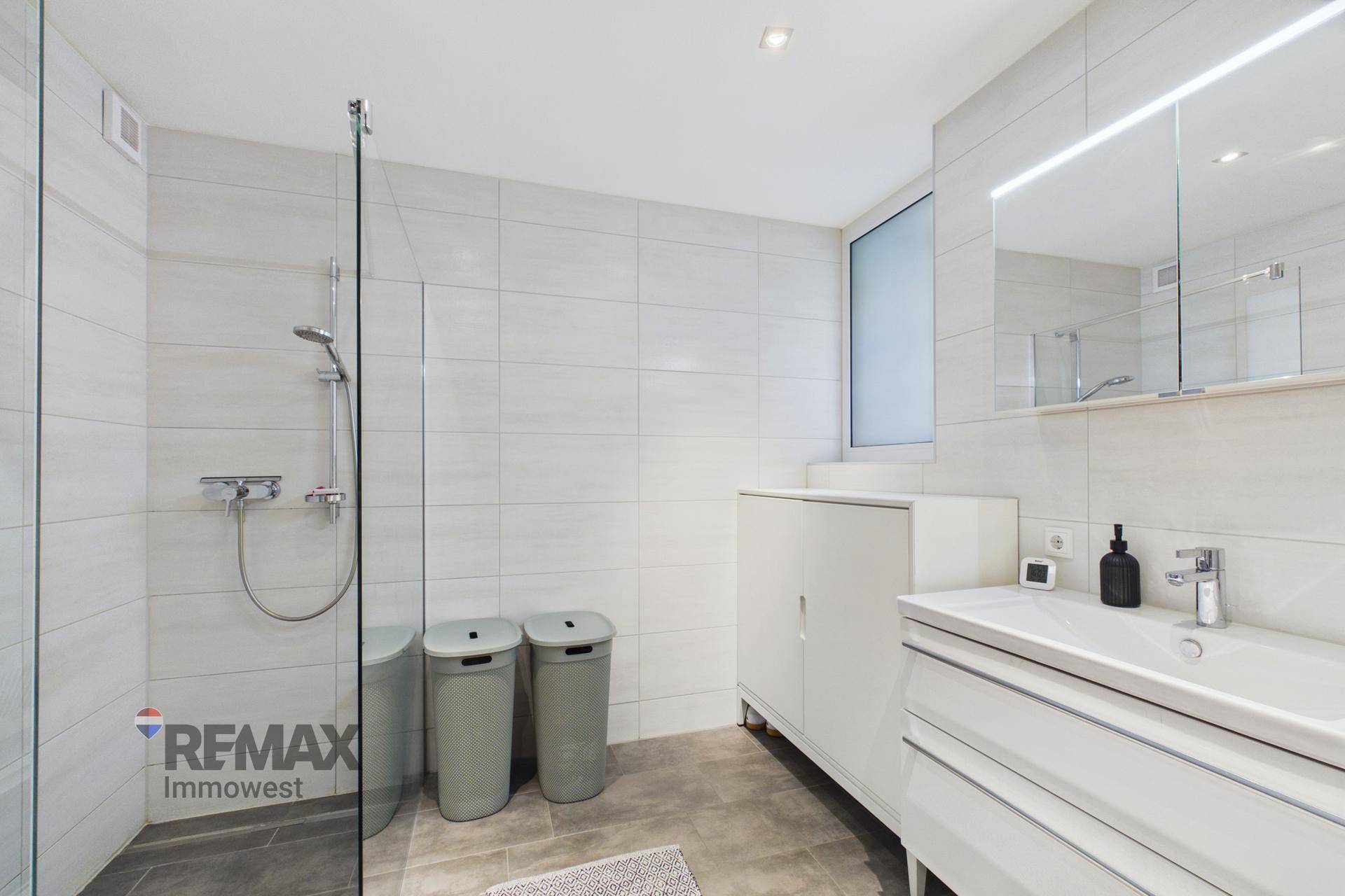 Modernes Badezimmer mit großer begehbarer Dusche, weißen Fliesen und Einzelwaschbecken.