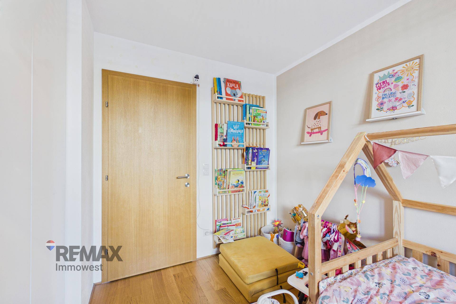 Kinderzimmer mit Holzboden, Bücherregal und einem kleinen Holzbett.
