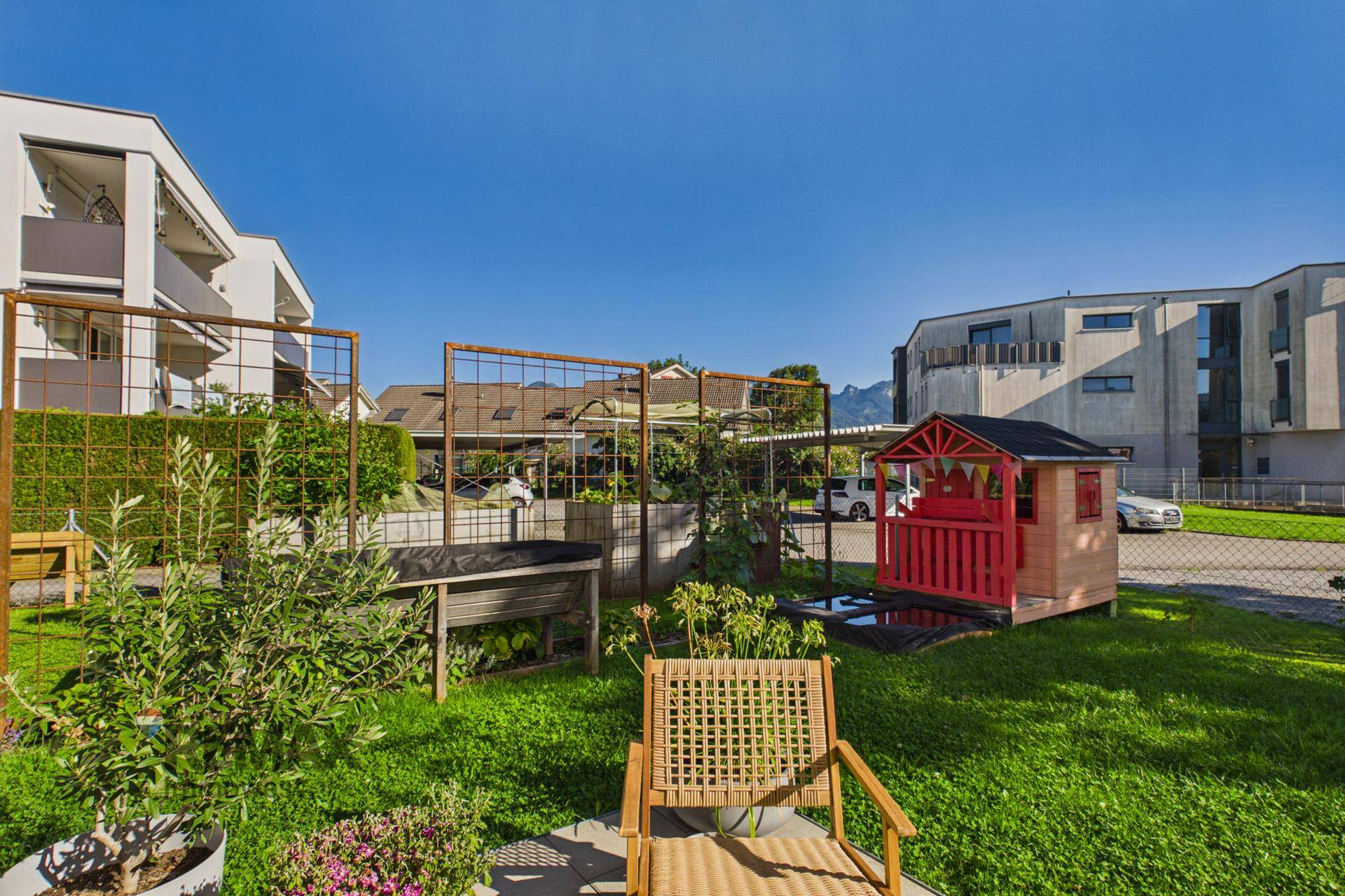Grüner Gartenbereich mit Spielhaus, Pflanzen und Blick auf die Umgebung.