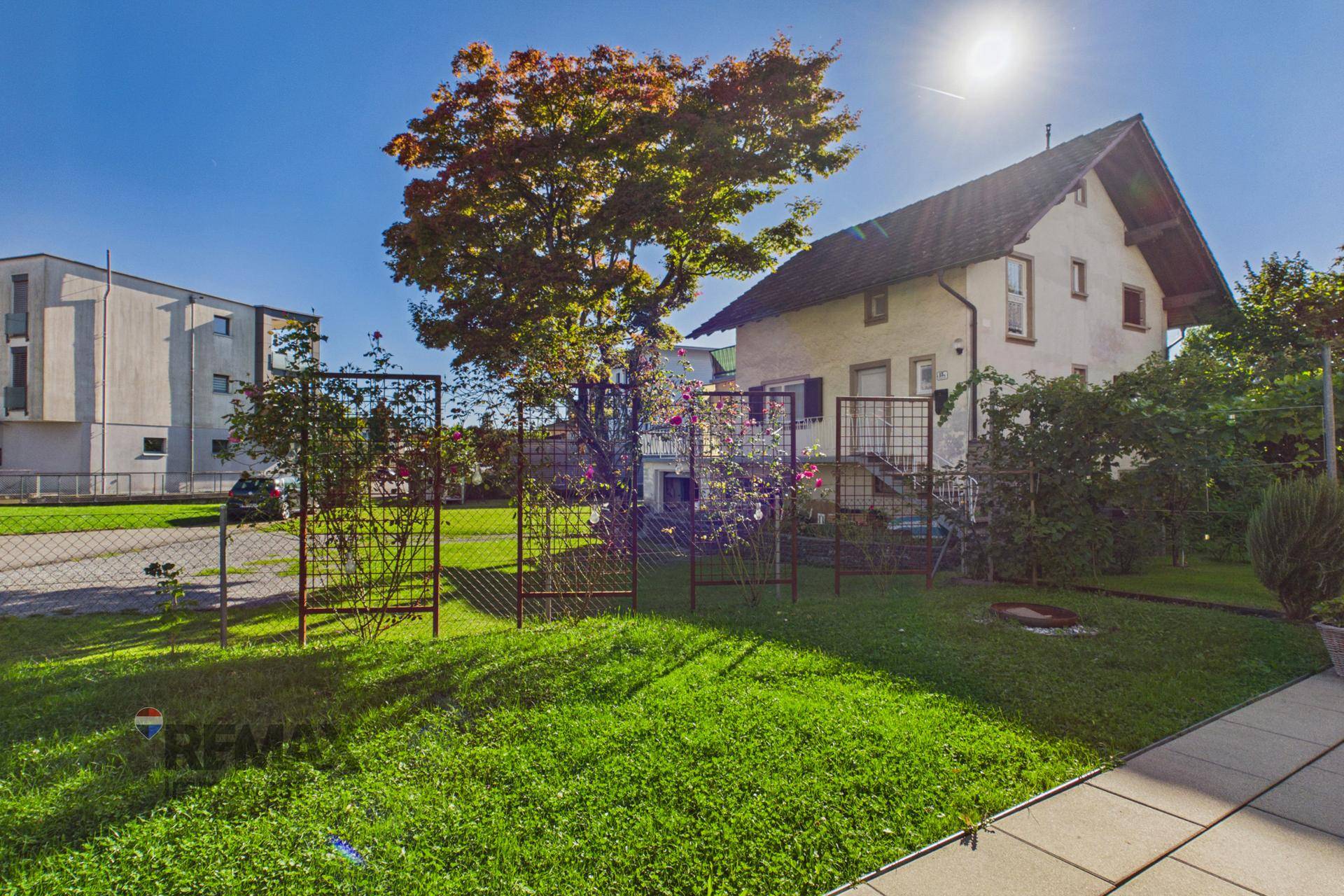 Gepflegter Garten mit Rasenfläche, Bäumen und einem traditionellen Haus im Hintergrund.